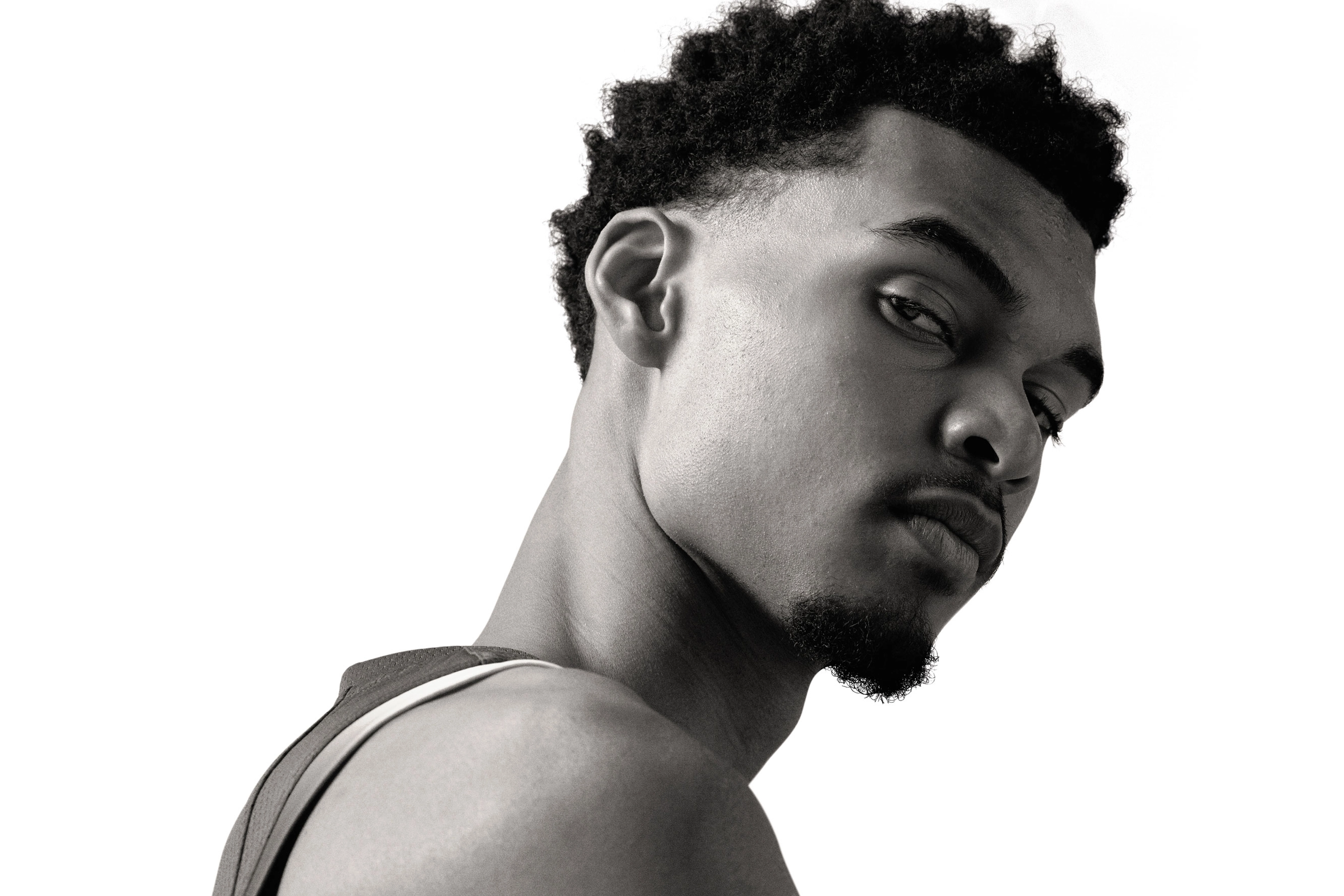 Black and white close up of Victor Wembanyama's face. He leans his head to the right, and looks across his shoulder to the camera.