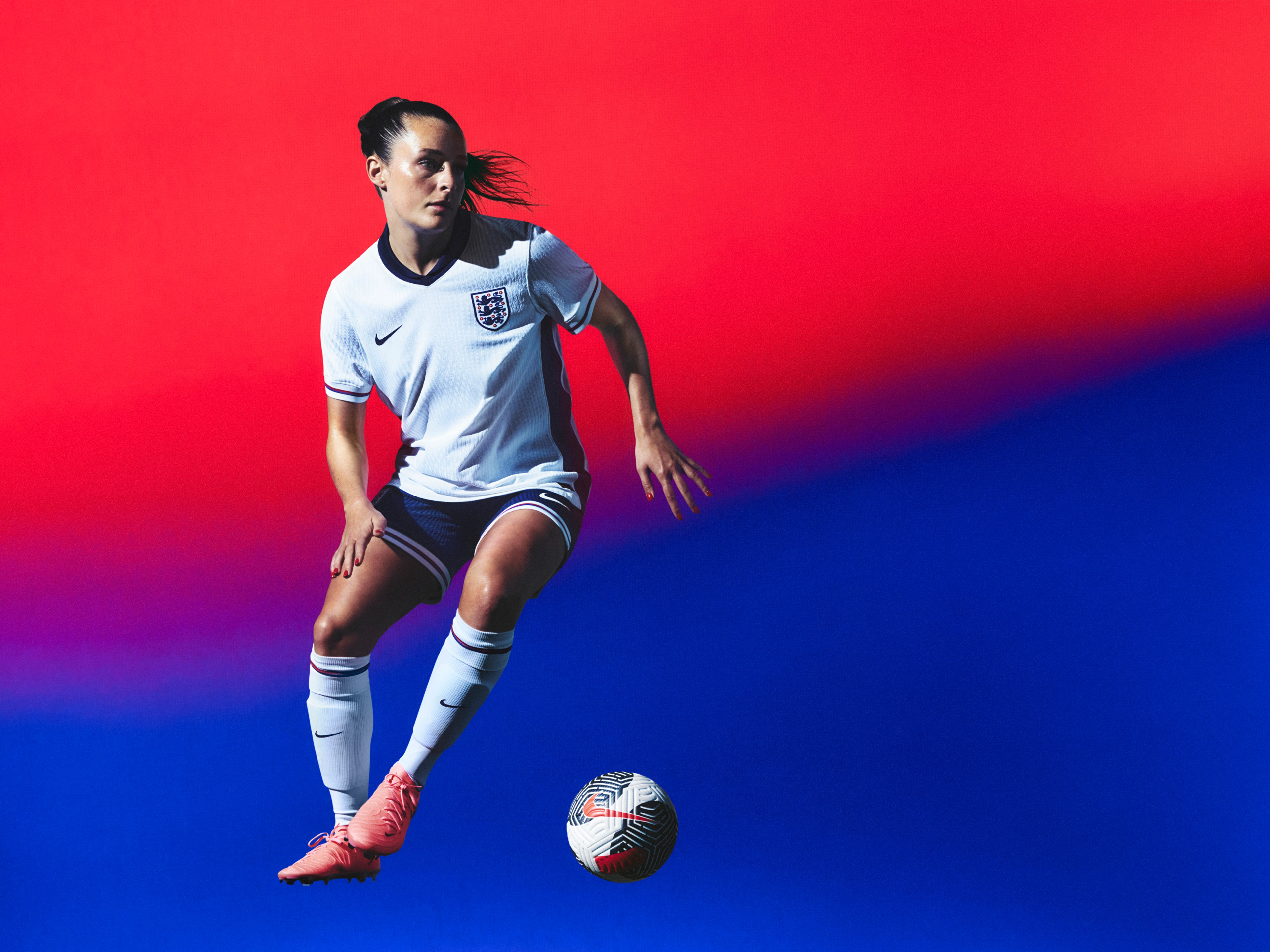 Athlete in a mid-kicking pose wearing a white soccer jersey with a navy blue collar and sides and red, white, and blue trim on the cuffs, as well as navy blue shorts with matching trim, each with a Nike swoosh and team logo on the chest and legs. They are also wearing white socks with matching trim.