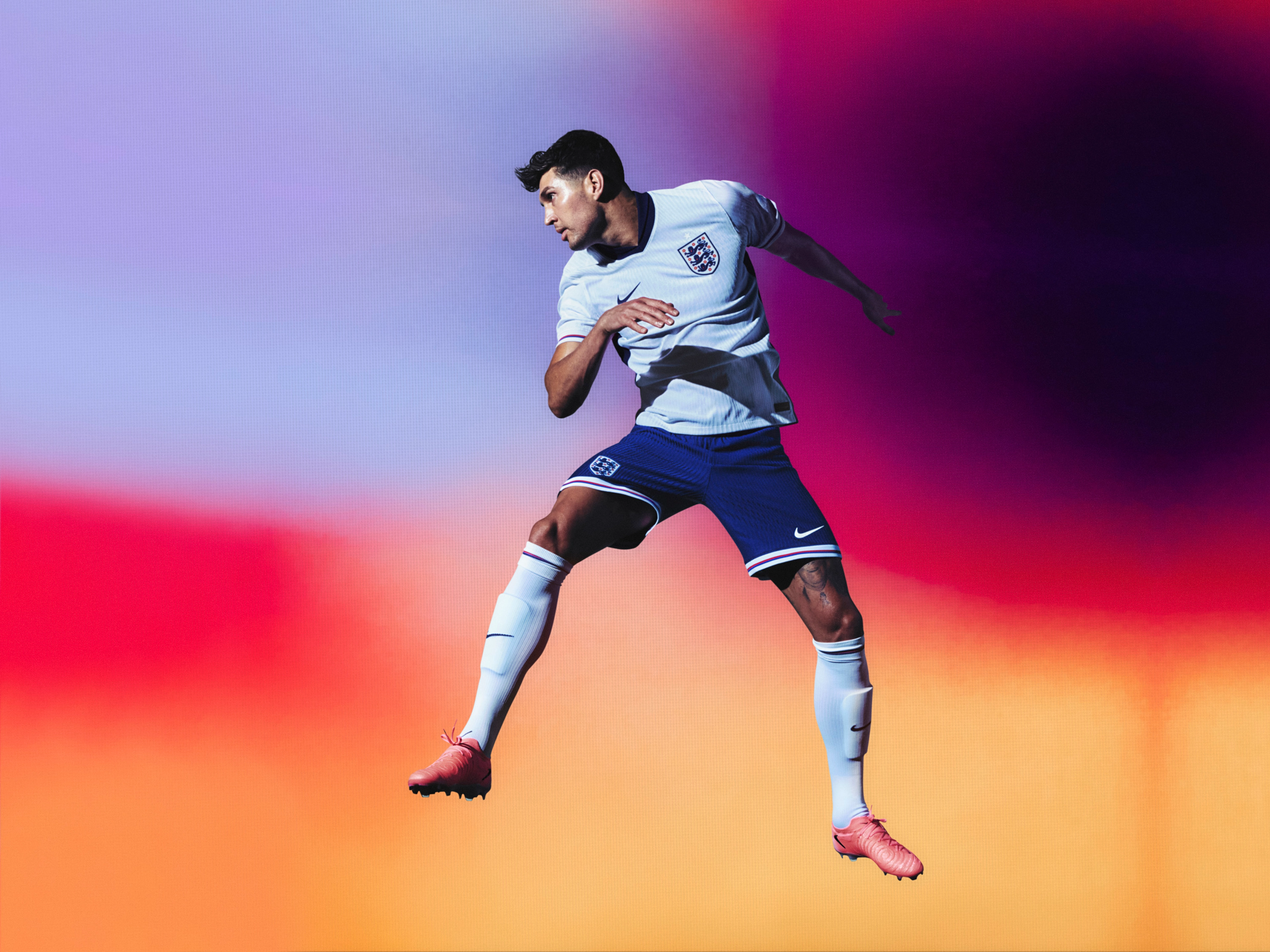 Athlete in a running pose wearing a white soccer jersey with a navy blue collar and sides and red, white, and blue trim on the cuffs, as well as navy blue shorts with matching trim, each with a Nike swoosh and team logo on the chest and legs. They are also wearing white socks with matching trim.