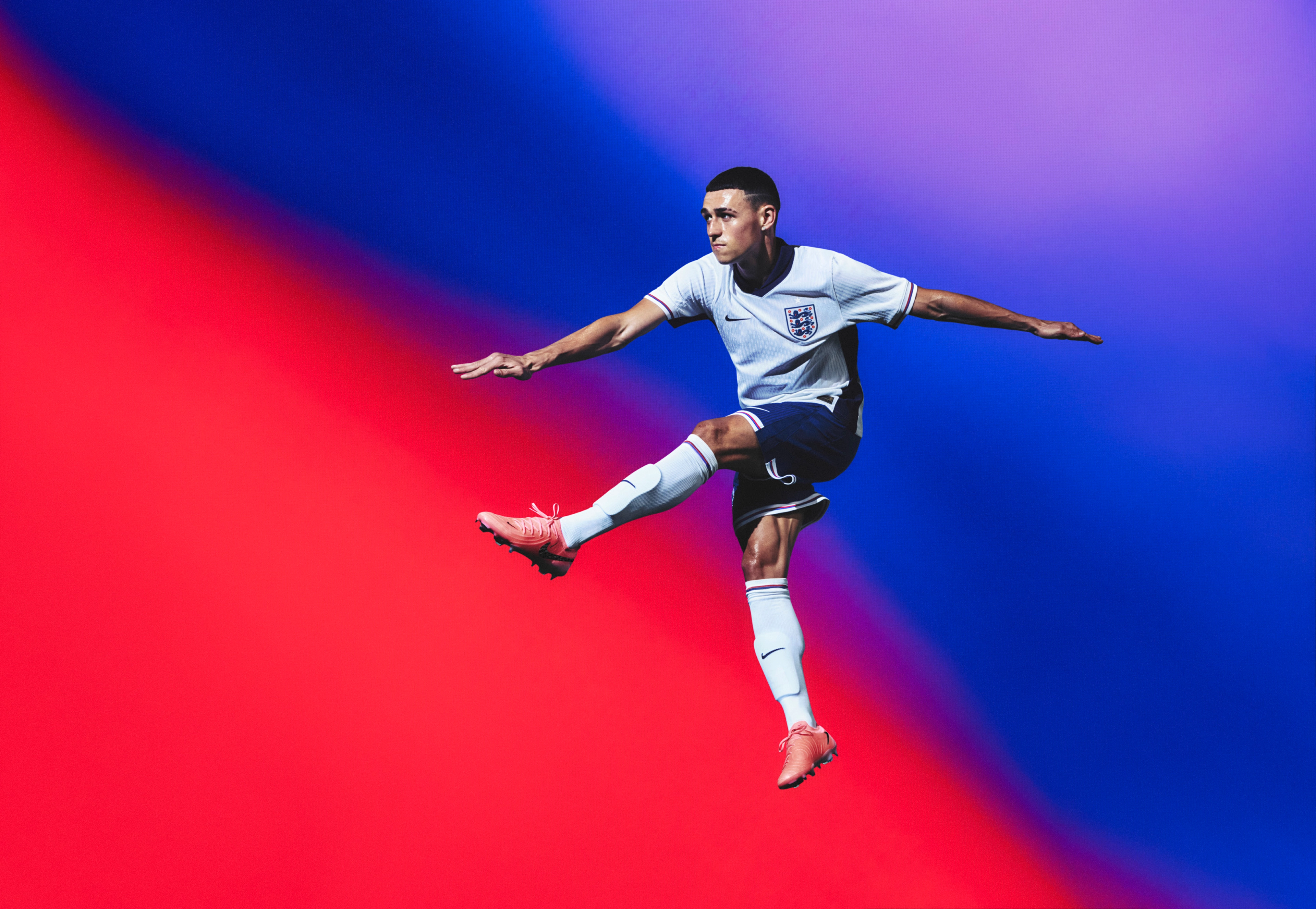 Athlete in a flying pose wearing a white soccer jersey with a navy blue collar and sides and red, white, and blue trim on the cuffs, as well as navy blue shorts with matching trim, each with a Nike swoosh and team logo on the chest and legs. They are also wearing white socks with matching trim.