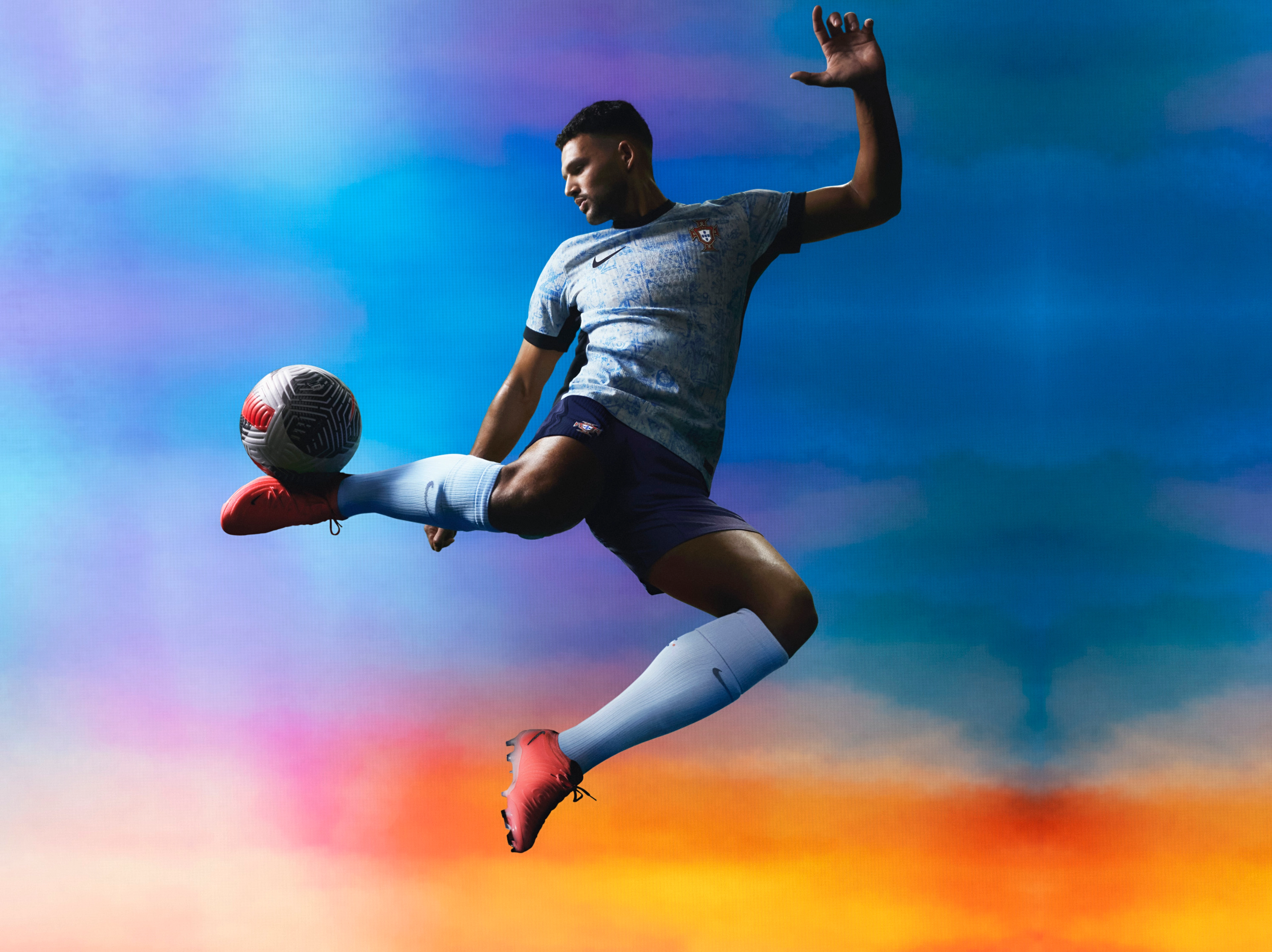 Athlete bouncing a soccer ball off their ankle wearing a white soccer jersey with black sides, a black collar, black cuffs, and a faded light blue triangle pattern, as well as matching black shorts, each with a Nike swoosh and team logo on the chest and legs. They are also wearing light grey socks.