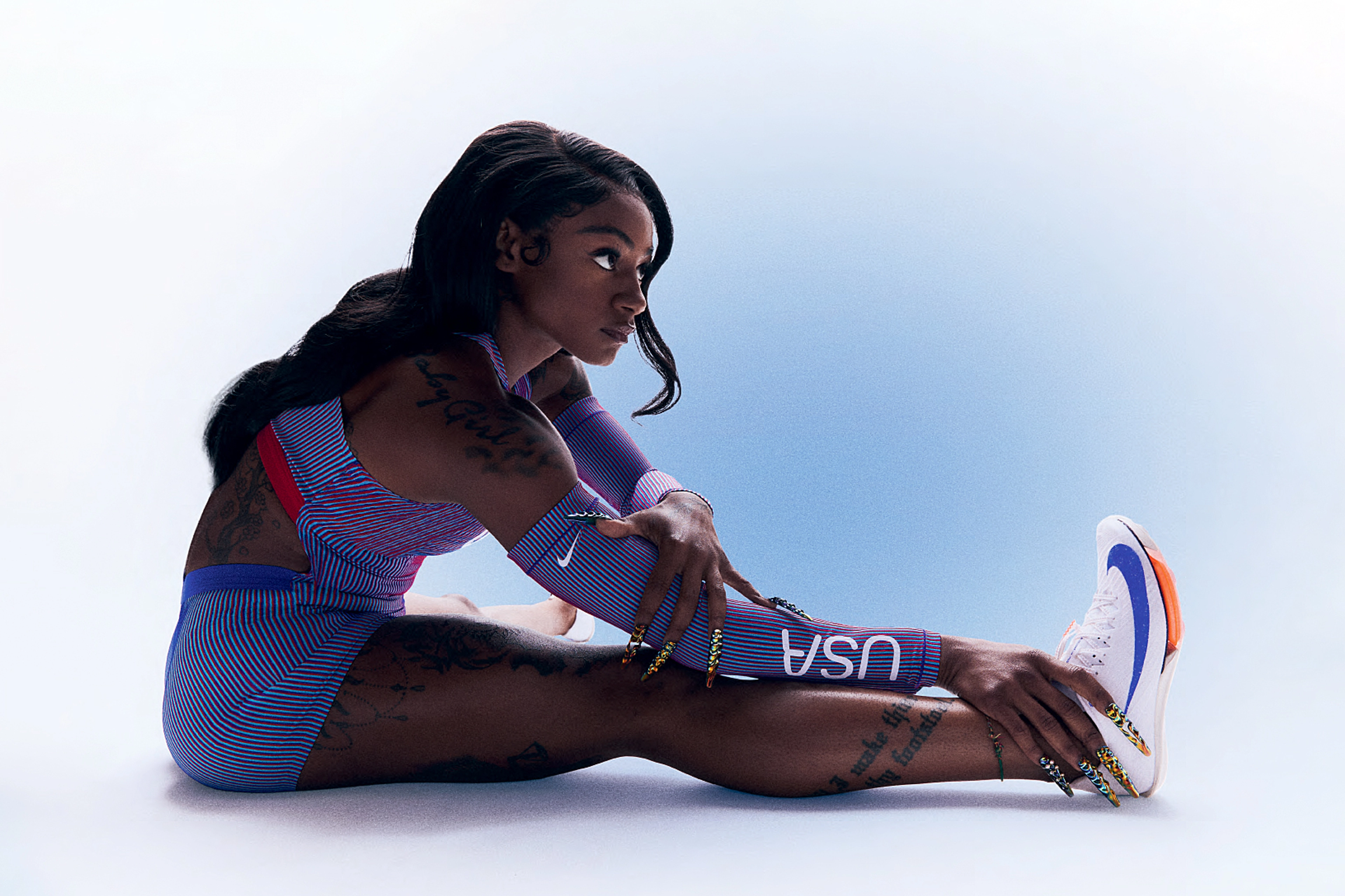 ShaCarri Richardson looks to the left as she sits stretching in her Team USA uniform.