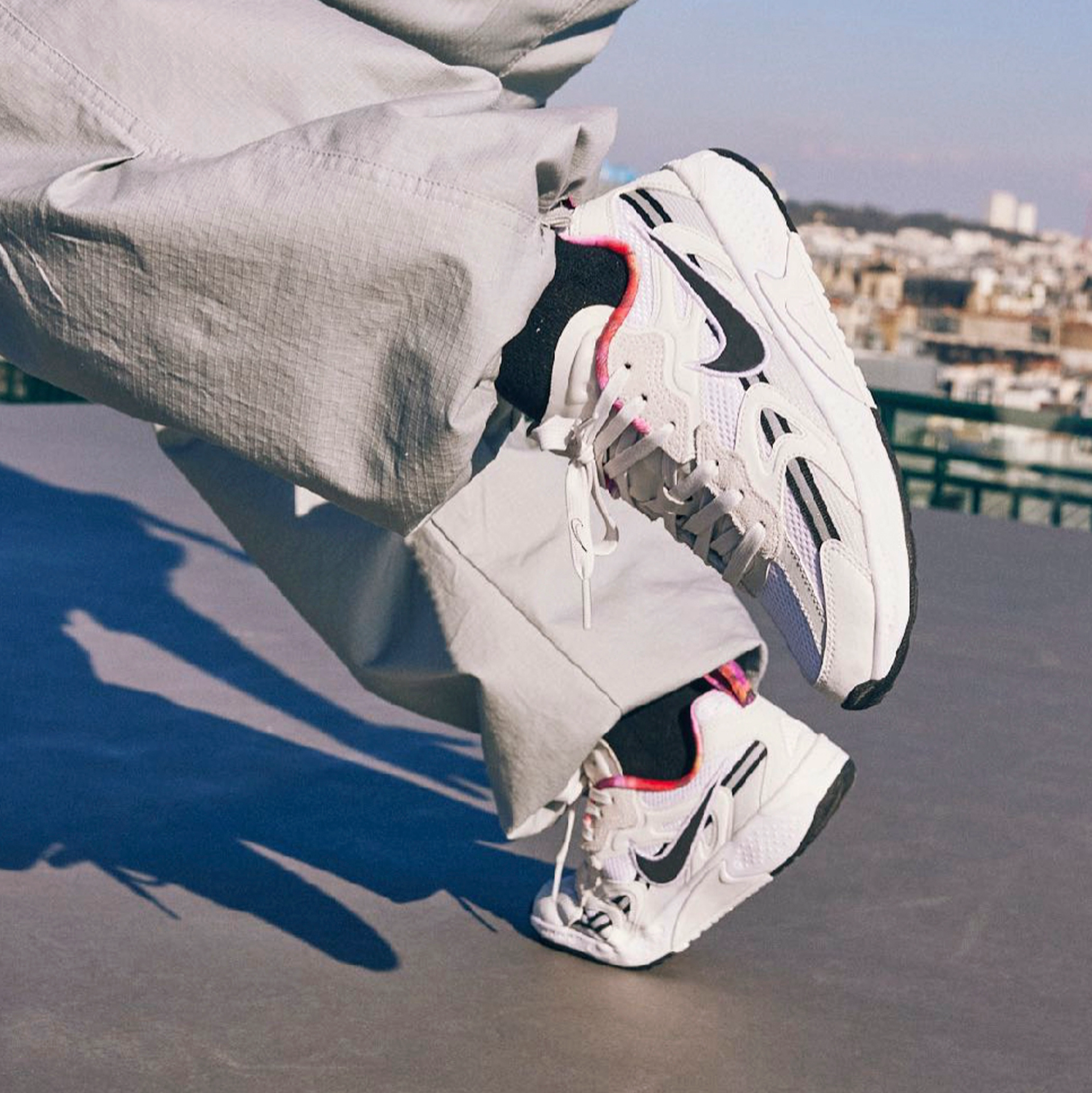 Legs in motion breakdancing, wear the Nike Jam sneaker, in a white and black colorway. The dancer is on a grey Paris rooftop, with a glimpse of the city showing behind them.