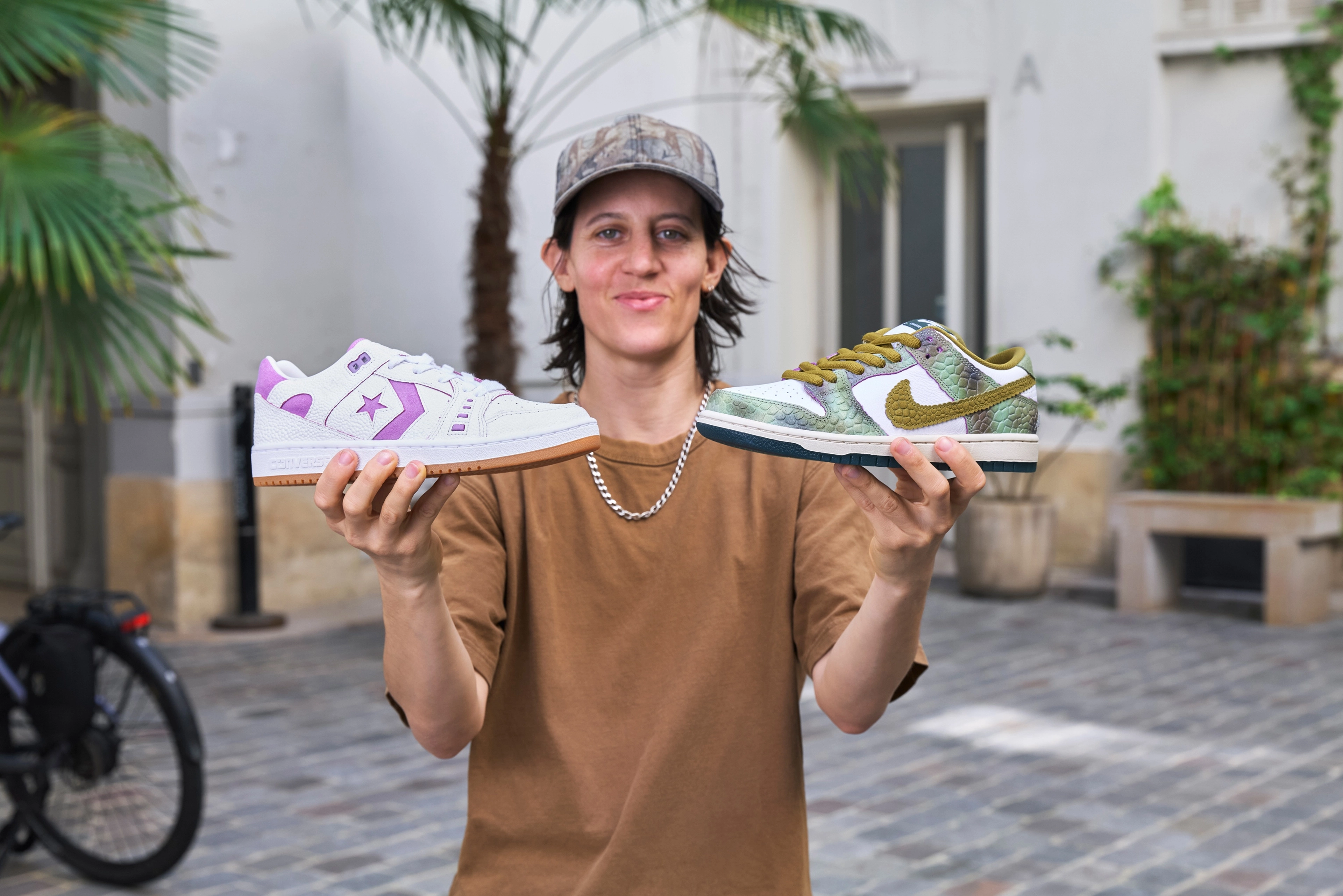 Converse CONS team rider Alexis Sable holding two shoes in her hands, on the right the Converse AS-1 Pro in purple and on the left the Nike SB Dunk Low in oil green and desert moss.