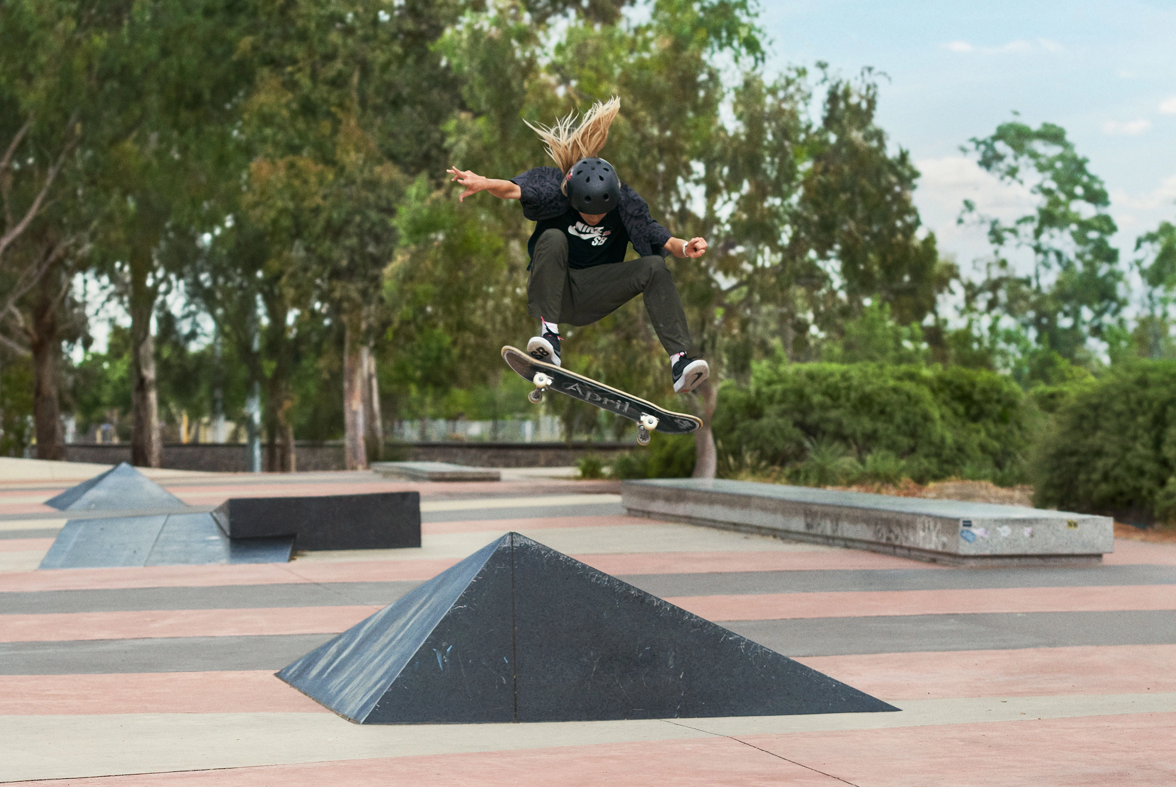 Male skateboarder doing a kick flip in the air with their skateboard  at a skate park while wearing the Nike SB Day One's in black.