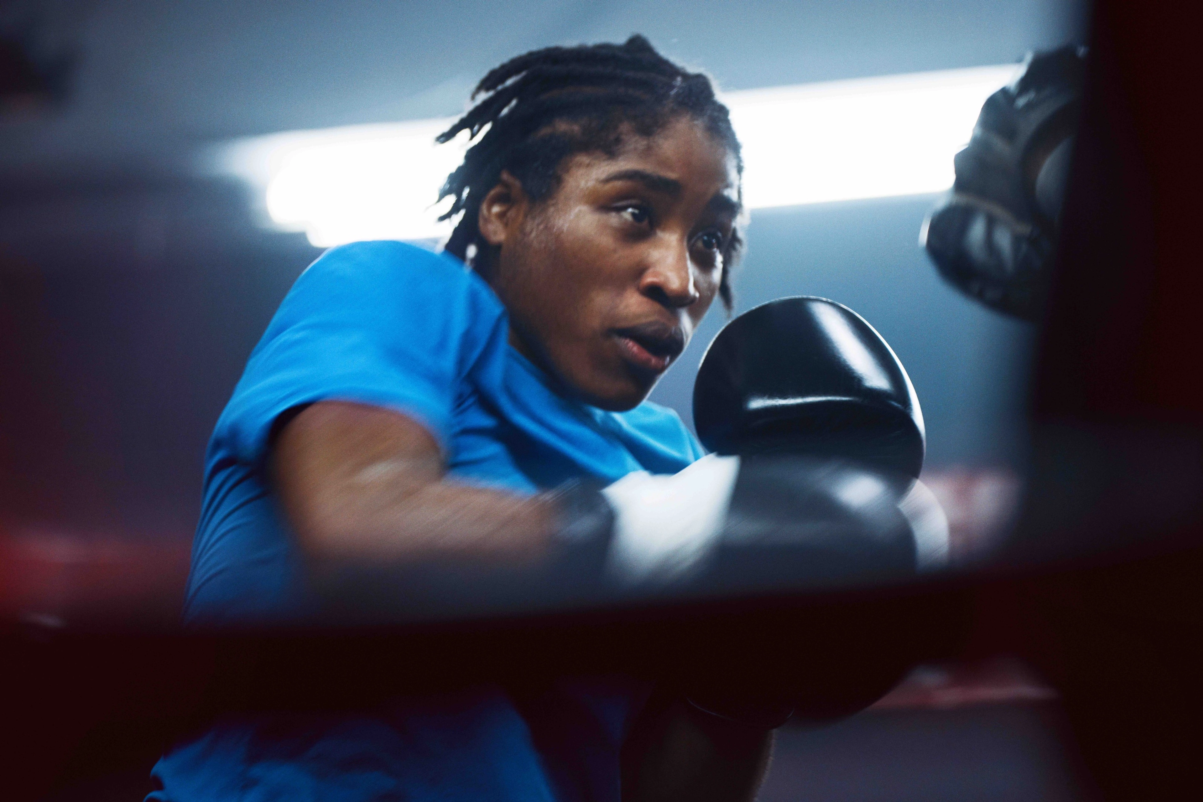 Cindy Ngamba in a blue shirt and black boxing gloves boxing an opponent that is out of the frame.