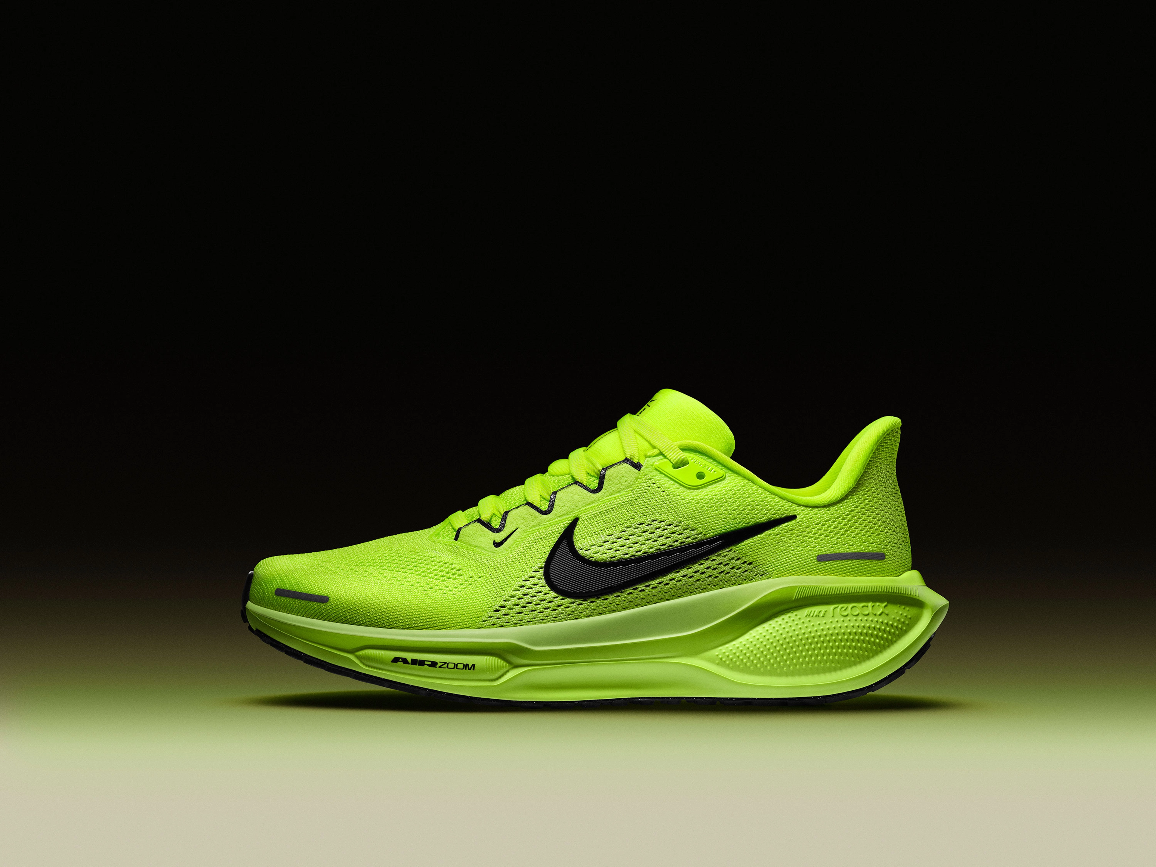 Left view of the Nike Pegasus 41 in the Volt green colorway. We see full-length ReactX foam and an Air Zoom Unit in the forefoot. There are reflectivity detail at the toe and heel. Volt upper, Barely Volt midsole, black sole, with a black Nike Swoosh. The shoe floats above a cream floor, with volt green glow against a dark background.