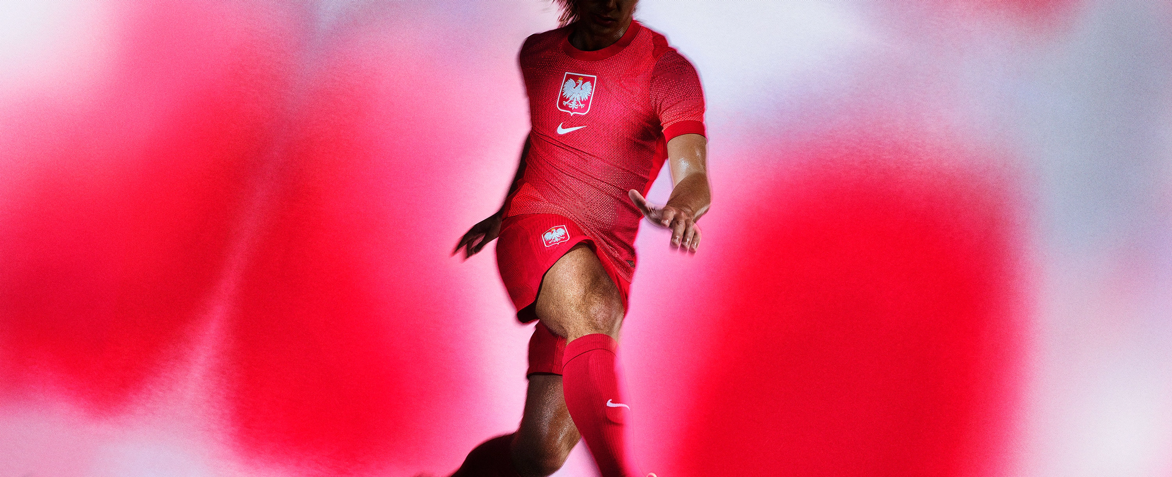 Athlete in a kicking pose wearing a red soccer jersey and matching red shorts with a Nike swoosh and logo on the chest and legs, as well as matching red socks.