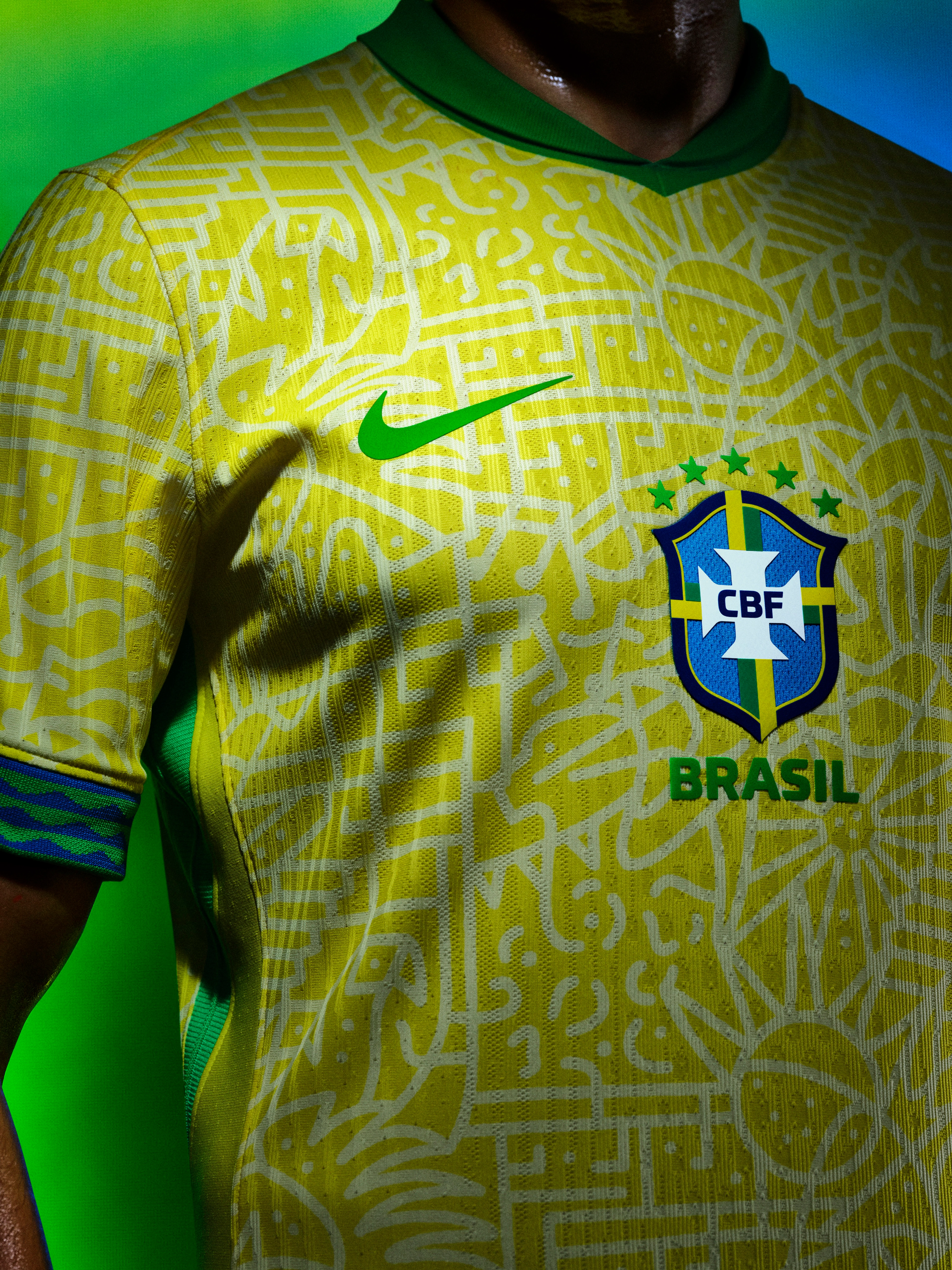 Close up view of an athlete's torso wearing a yellow soccer jersey with jade green trim on the cuffs and collar, featuring white doodle patterns, a green Nike swoosh on the right side of the chest, and a team logo in the center.