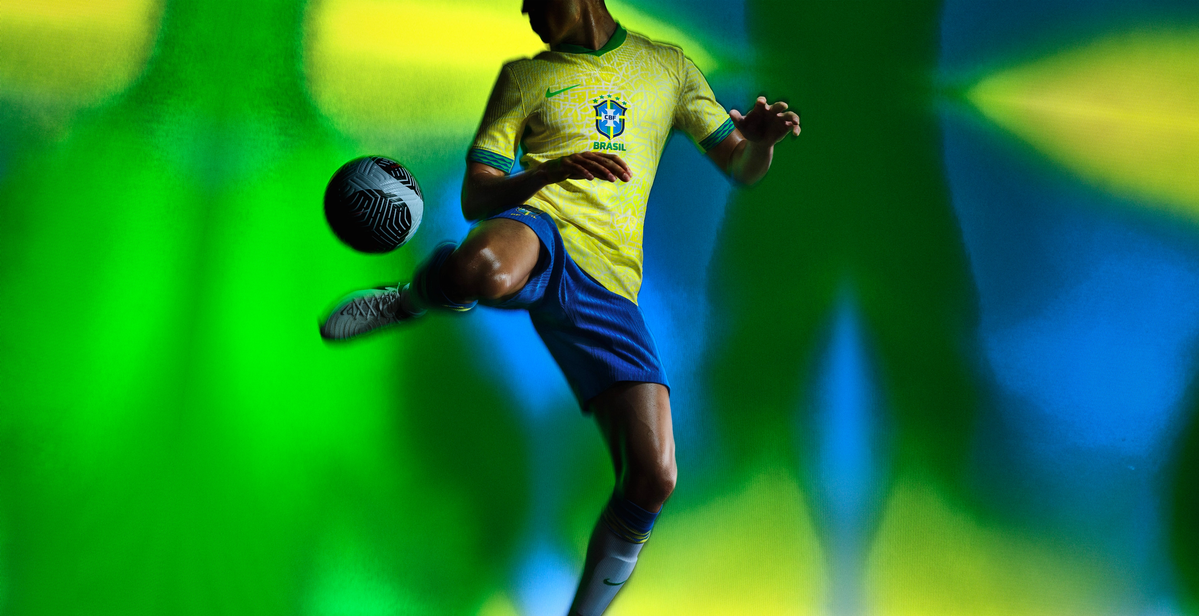 Athlete bouncing a soccer ball off their heel wearing a yellow soccer jersey with jade green trim on the cuffs and collar, as well as cobalt blue shorts, each with a Nike swoosh and team logo on the chest and legs.