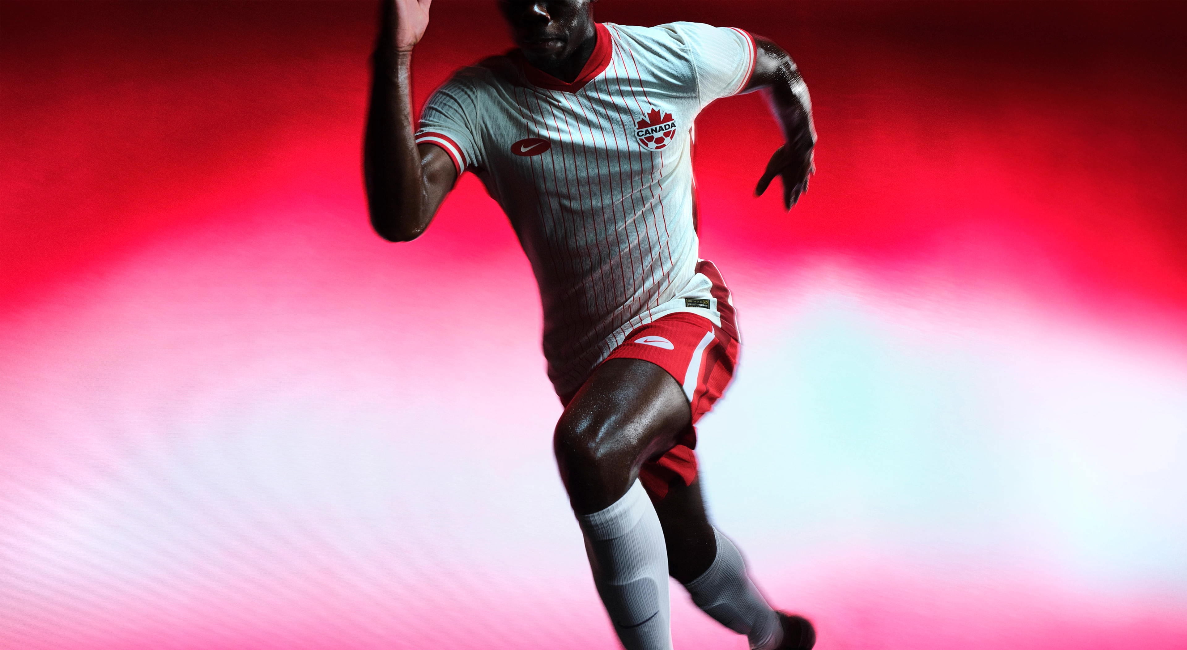 Athlete in a sprinting pose wearing a white soccer jersey with red pinstripes and red and white striped trim on the collar and cuffs, as well as red shorts with a red and white stripe on the side, each with a Nike swoosh and team logo on the chest and legs.