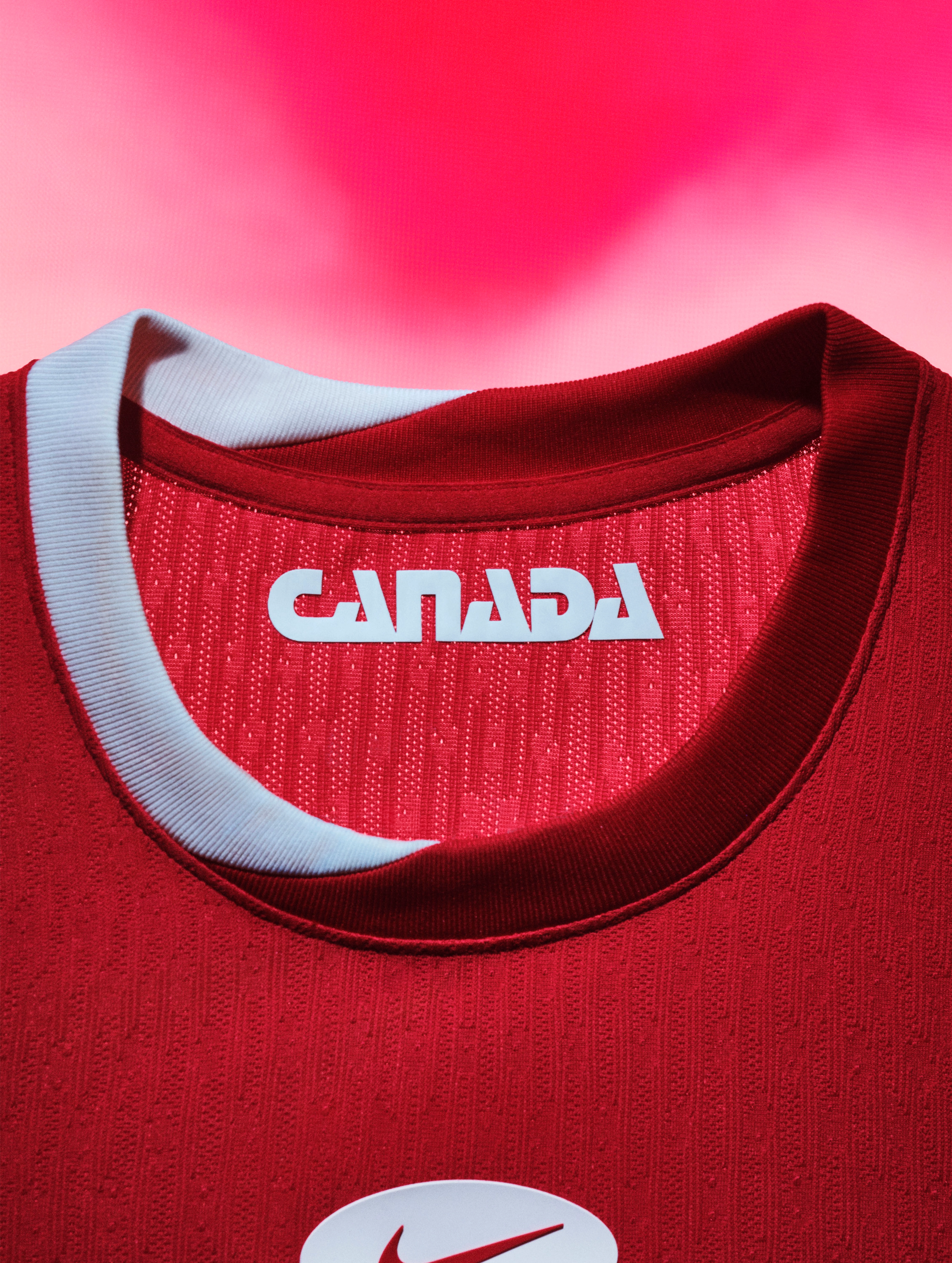 Close up view of a red soccer jersey collar with red and white striped trim and "Canada" printed in white on the inside.