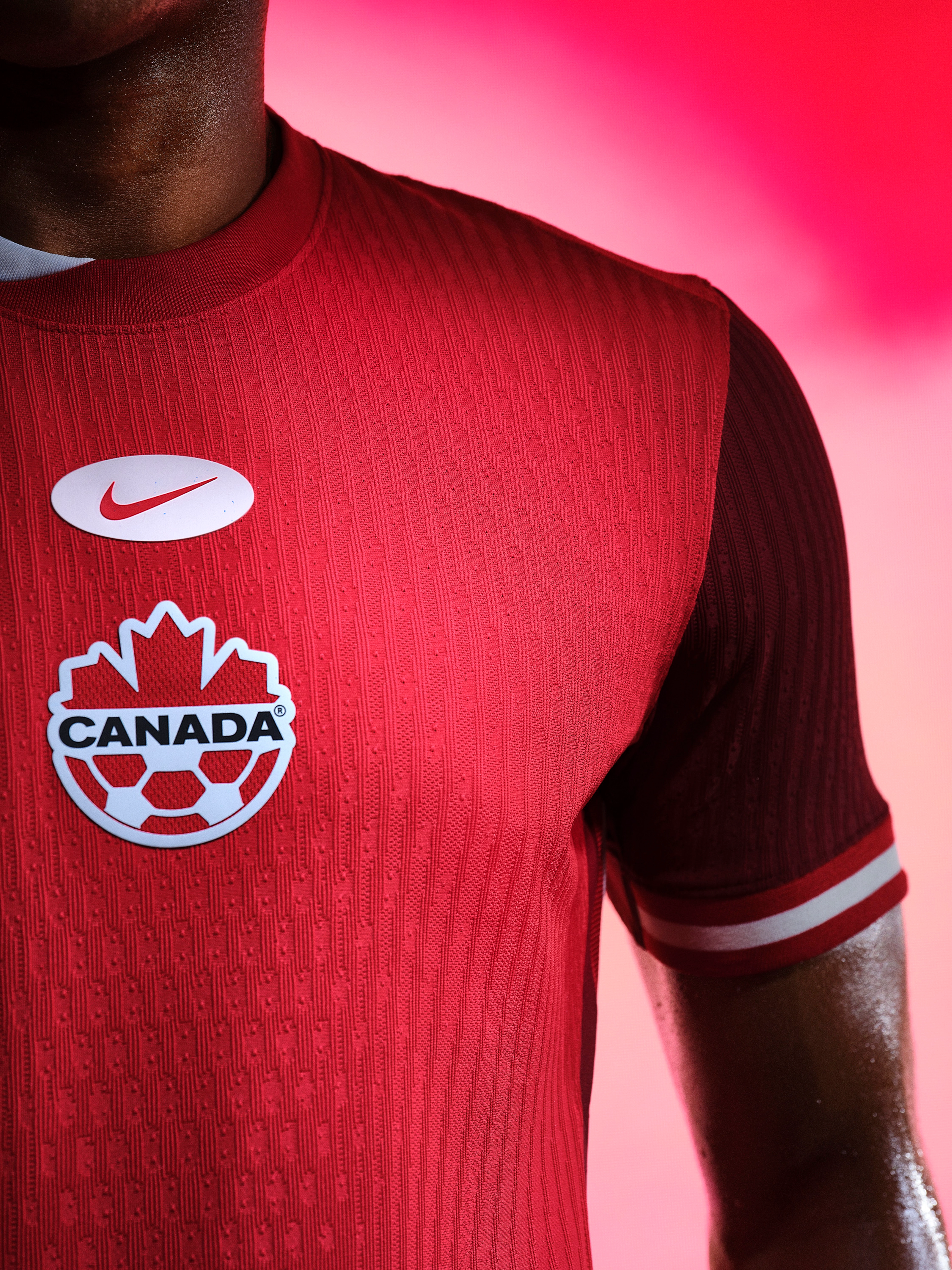 Close up view of an athlete's torso wearing a red soccer jersey with red and white striped trim on the collar and cuffs and a Nike swoosh and team logo centered on the chest.