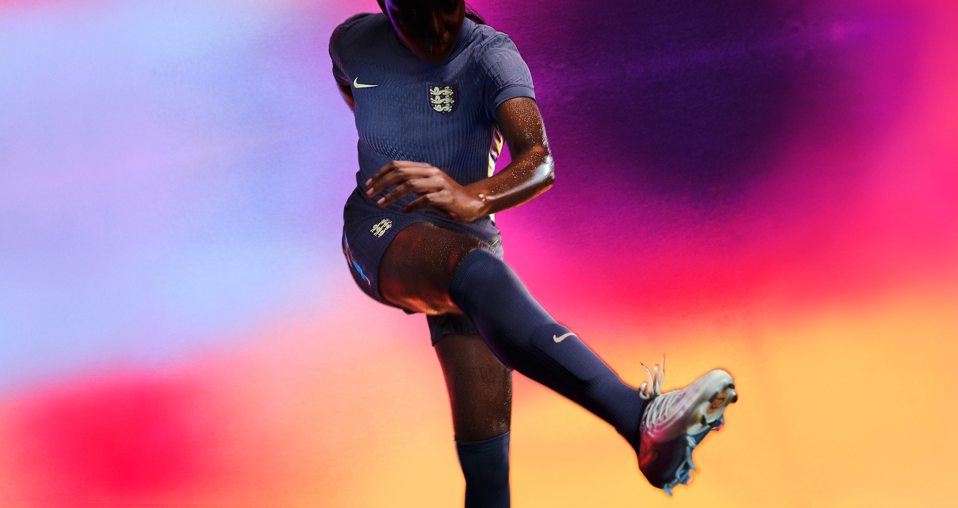 Athlete in a kicking pose wearing a navy blue soccer jersey and matching navy blue shorts, each with a Nike swoosh and team logo on the chest and legs. They are also wearing matching navy blue socks.