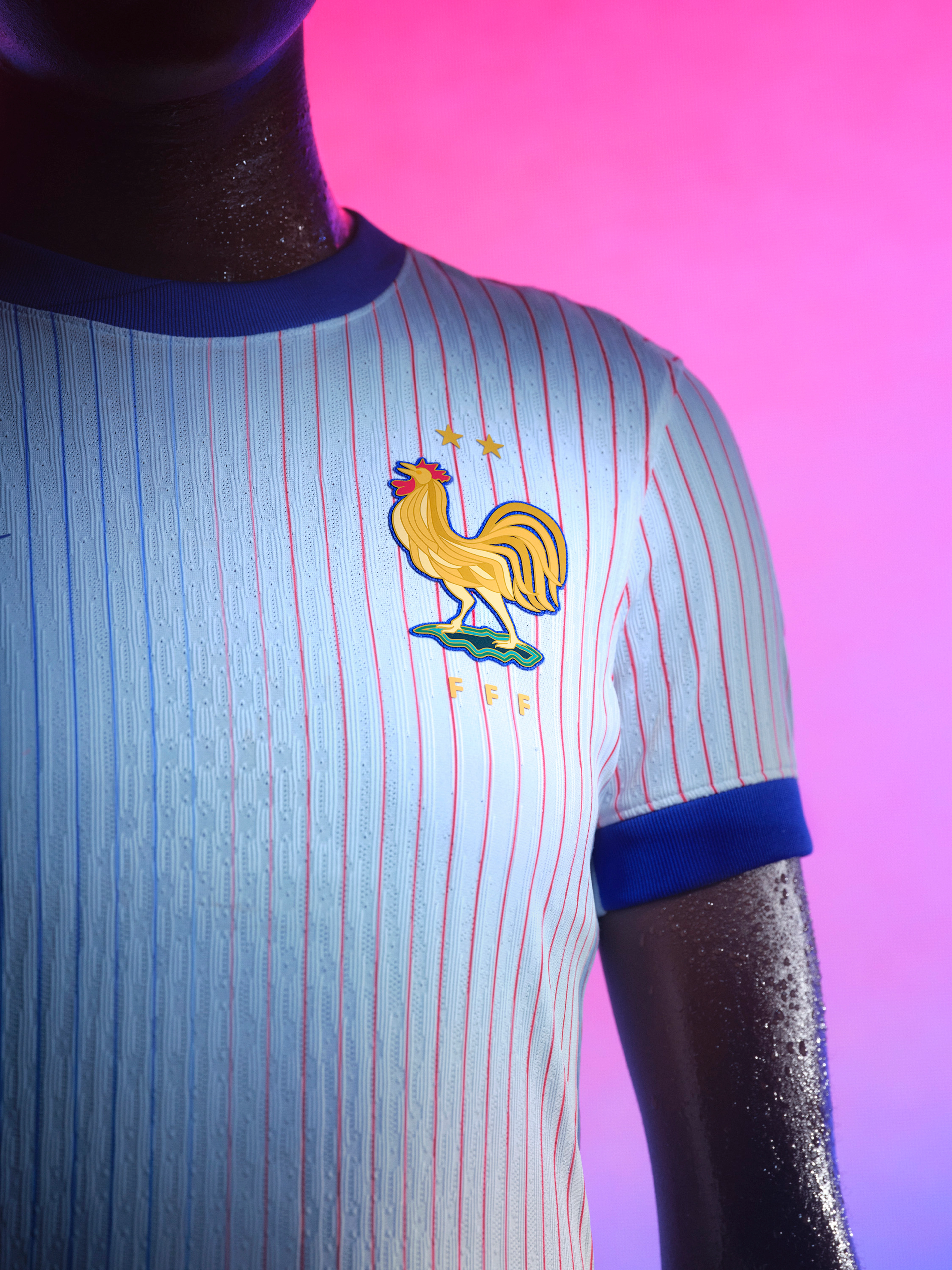 Close up view of the left side of an athlete's torso wearing a white soccer jersey with red and blue pinstripes, a blue collar and cuffs, and a team logo on the left side of the chest.