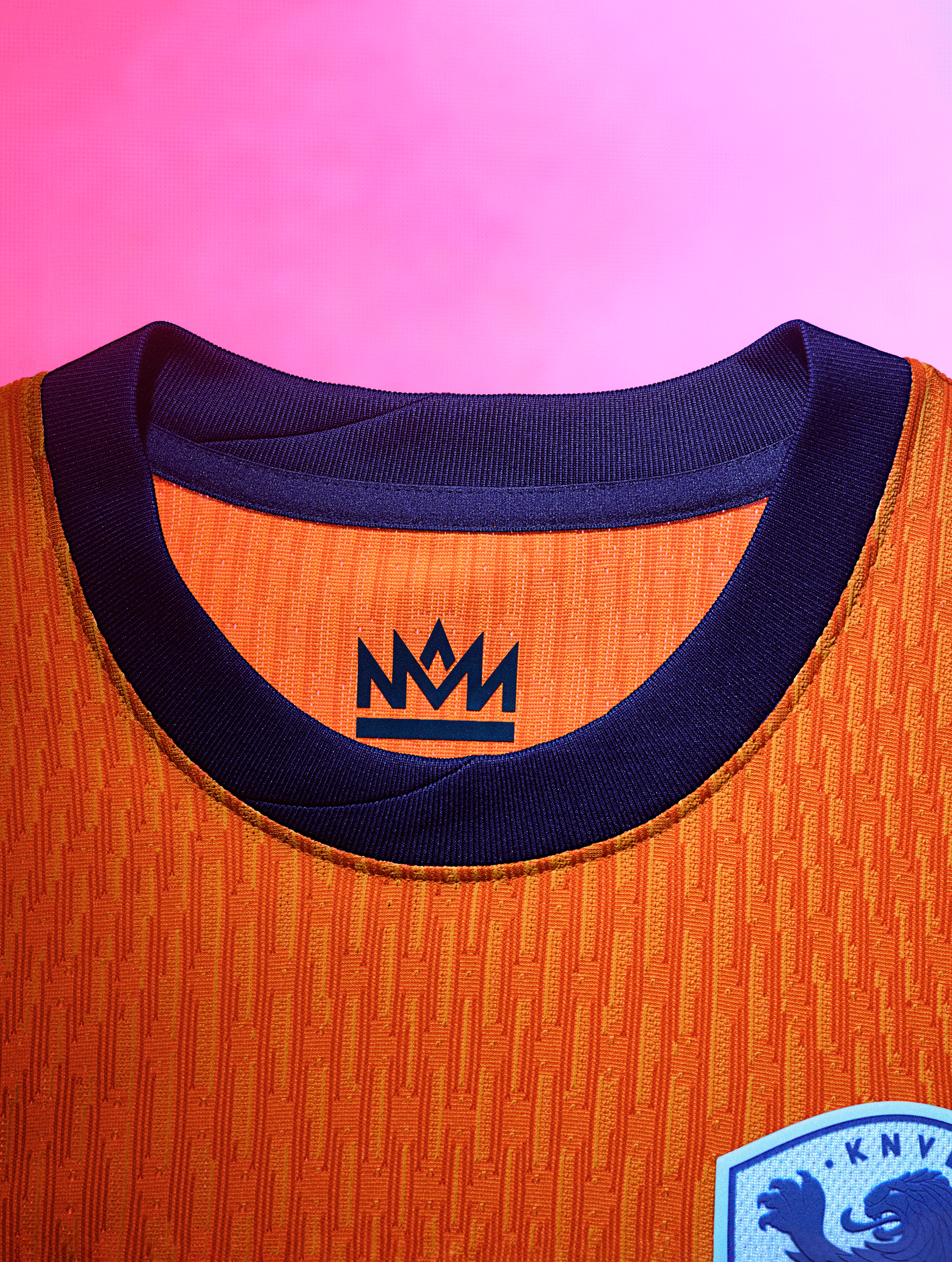 Close up view of an orange soccer jersey collar with an indigo collar and a logo on the back.