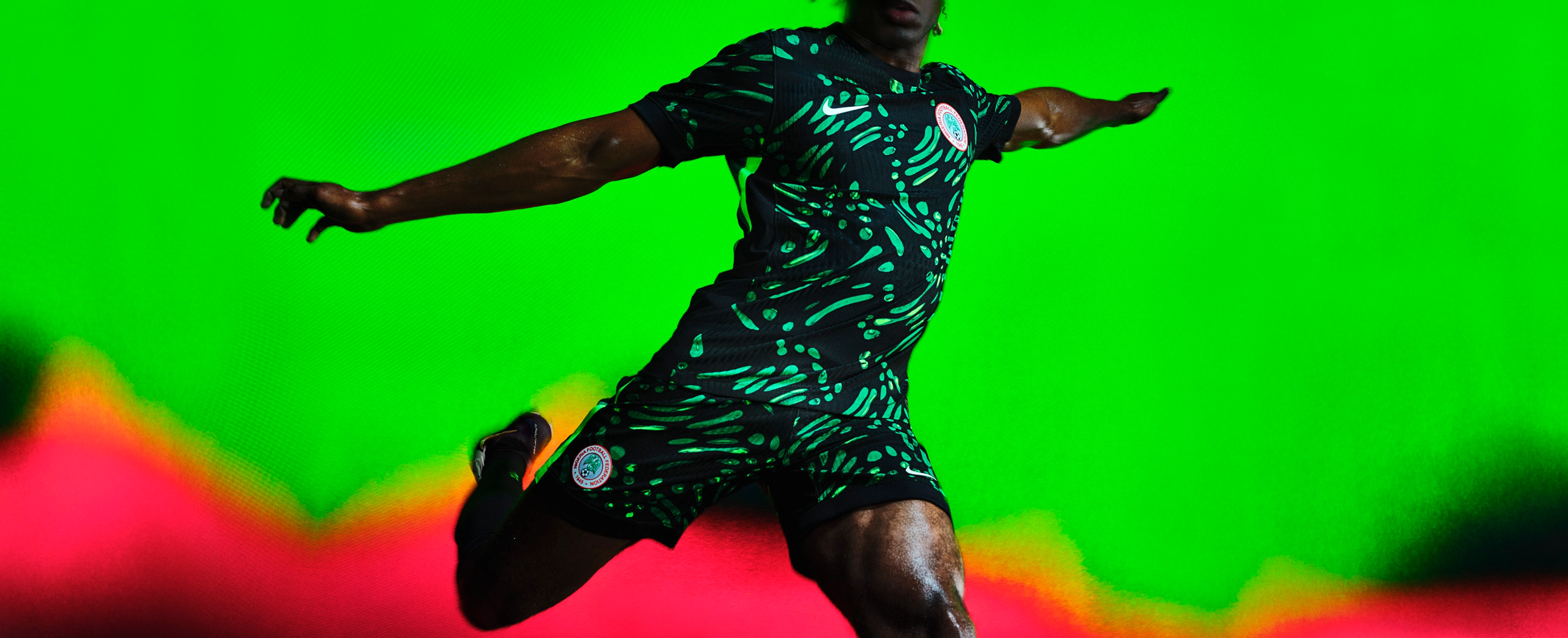Athlete in a mid-kicking pose wearing a black soccer jersey with neon green spots and streaks, as well as matching black shorts with neon green spots and streaks, each with a Nike swoosh and team logo on the chest and legs.