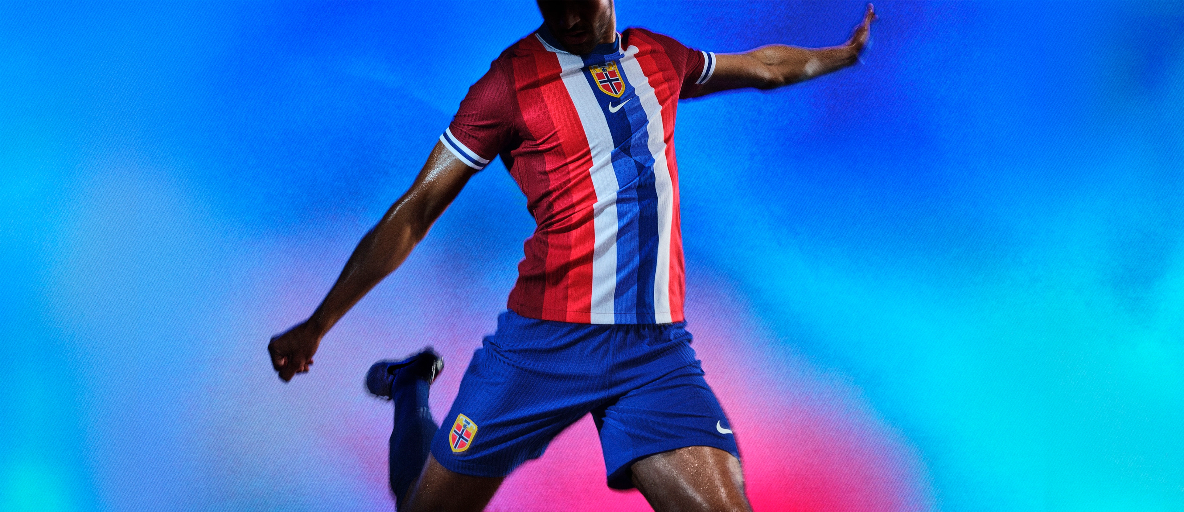 Athlete in a mid-kicking pose wearing a soccer jersey with red, white, and blue vertical stripes, as well as matching blue shorts, each with a Nike swoosh and team logo on the chest and legs.