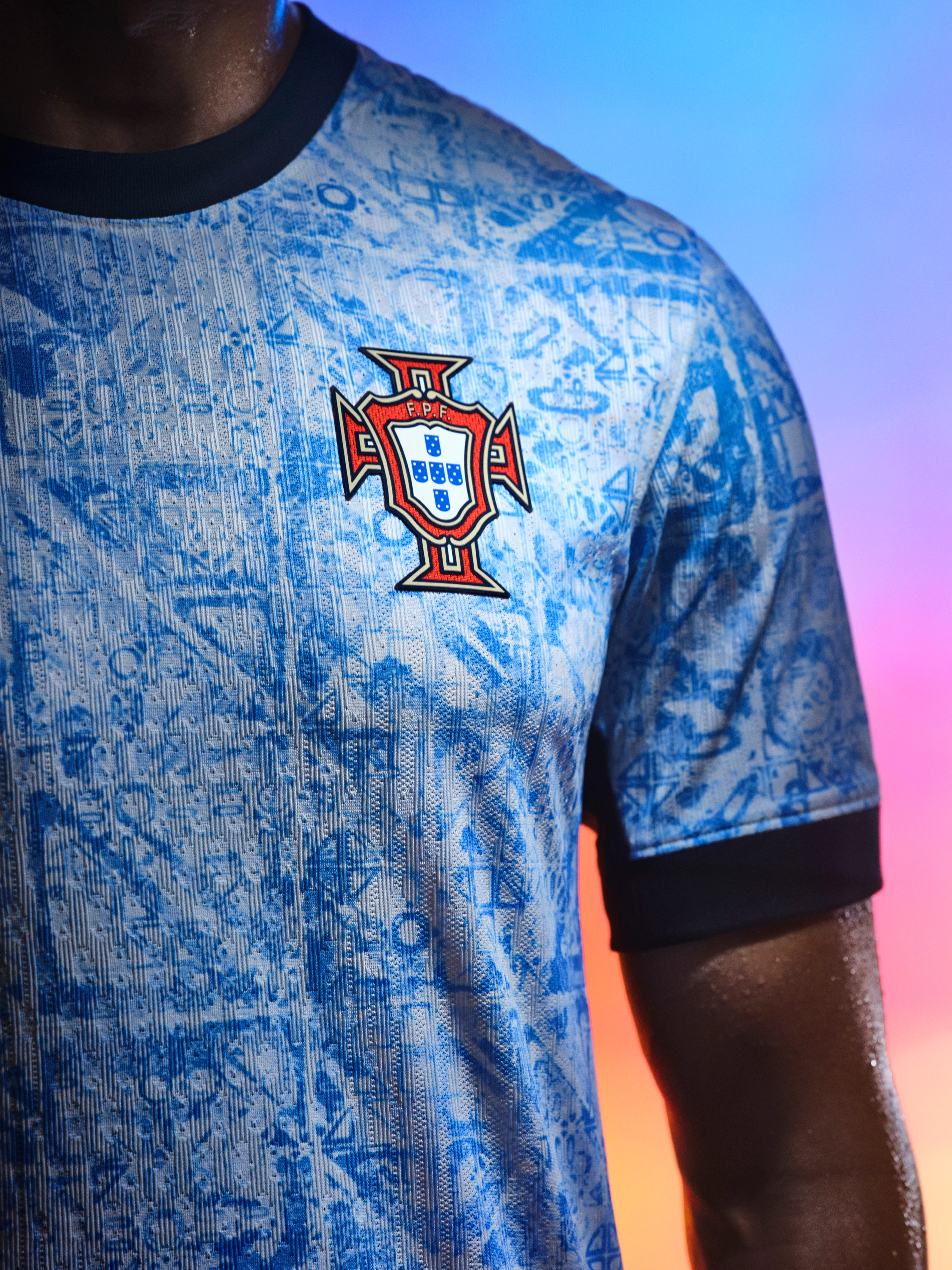 Close up view of an athlete's torso wearing a white jersey with faded light blue triangle patterns, black cuffs, a black collar, and a team logo on the left side of the chest.