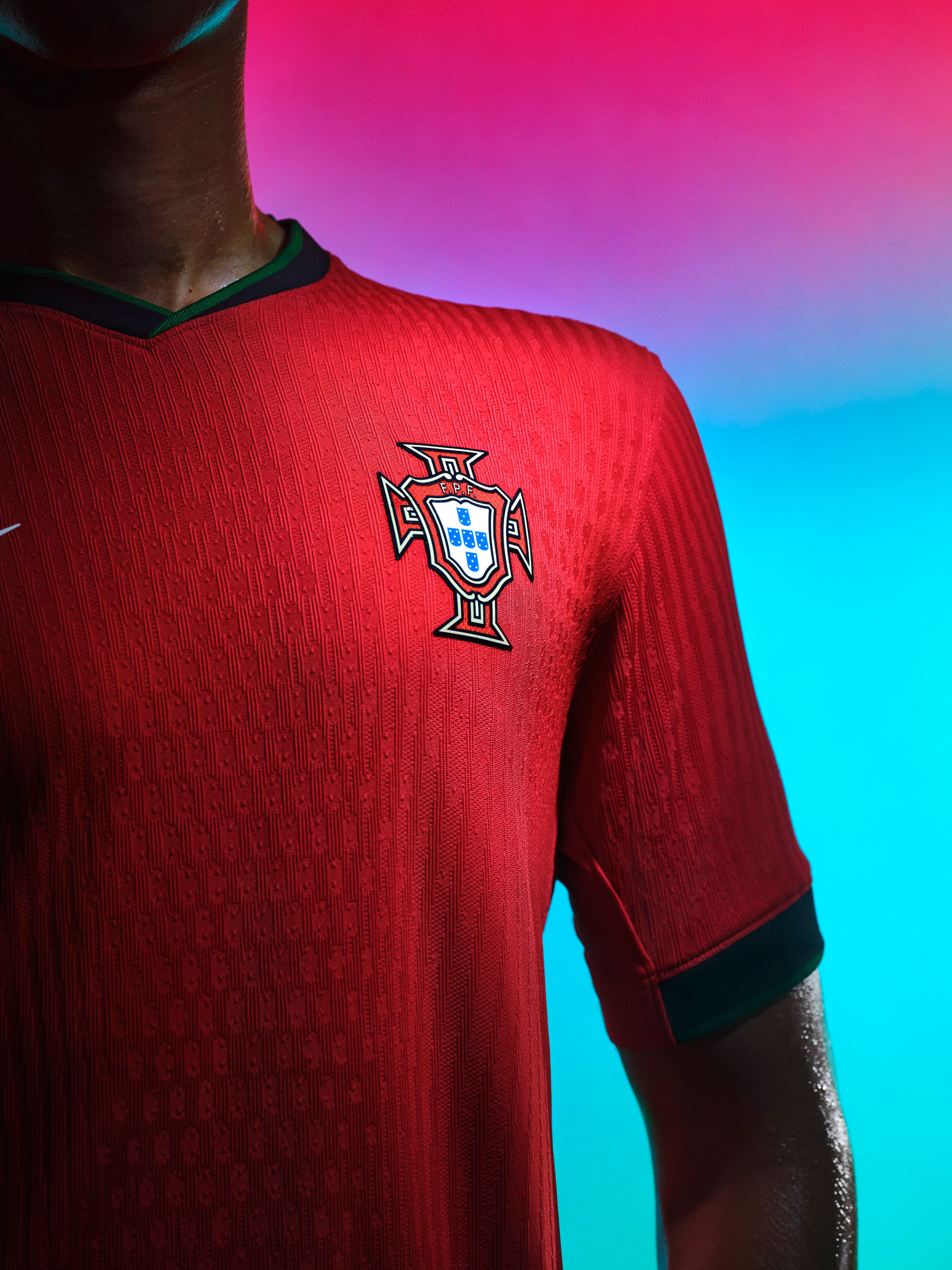 Close up view of an athlete's torso wearing a red soccer jersey with a forest green collar, forest green cuffs, and a team logo on the left side of the chest.