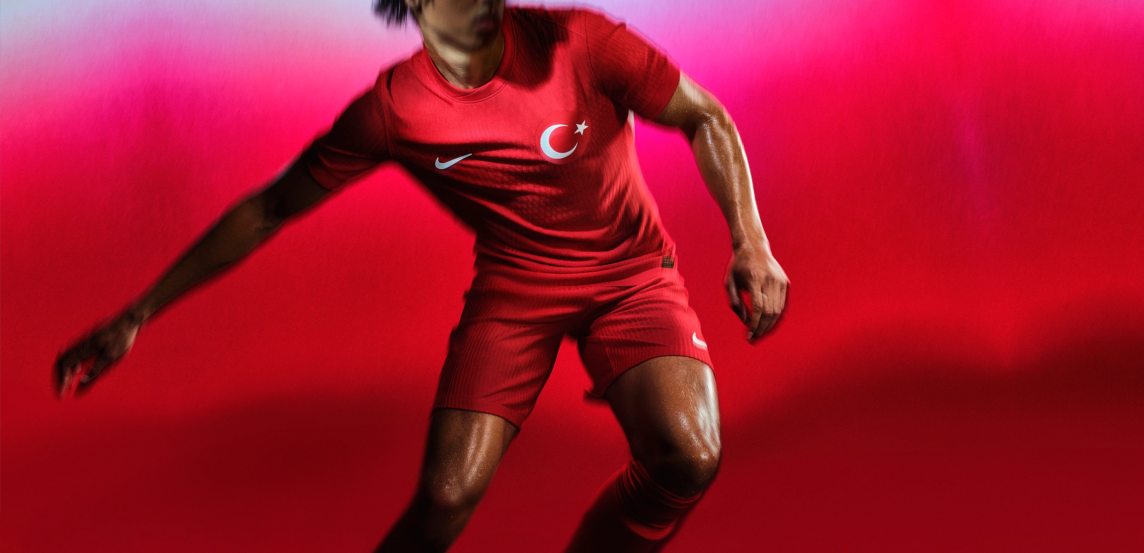Athlete dribbling a soccer ball wearing a red soccer jersey with matching red shorts, each with a Nike swoosh on the chest and legs and a team logo on the chest.