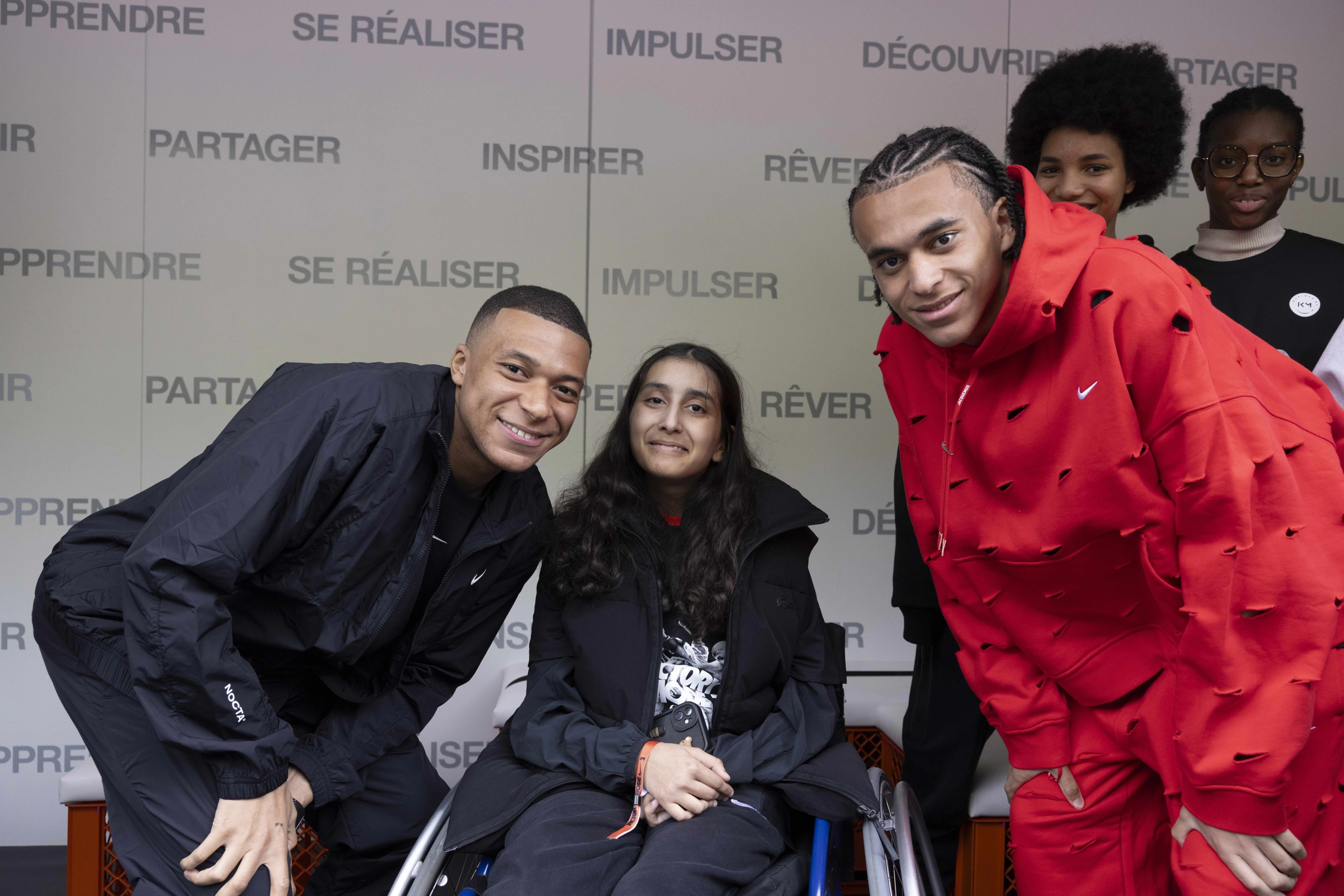 Kylian and Ethan Mbappe pose with a young athlete in a wheelchair, while other young athletes look on at the Victory Mode event in Paris, France.