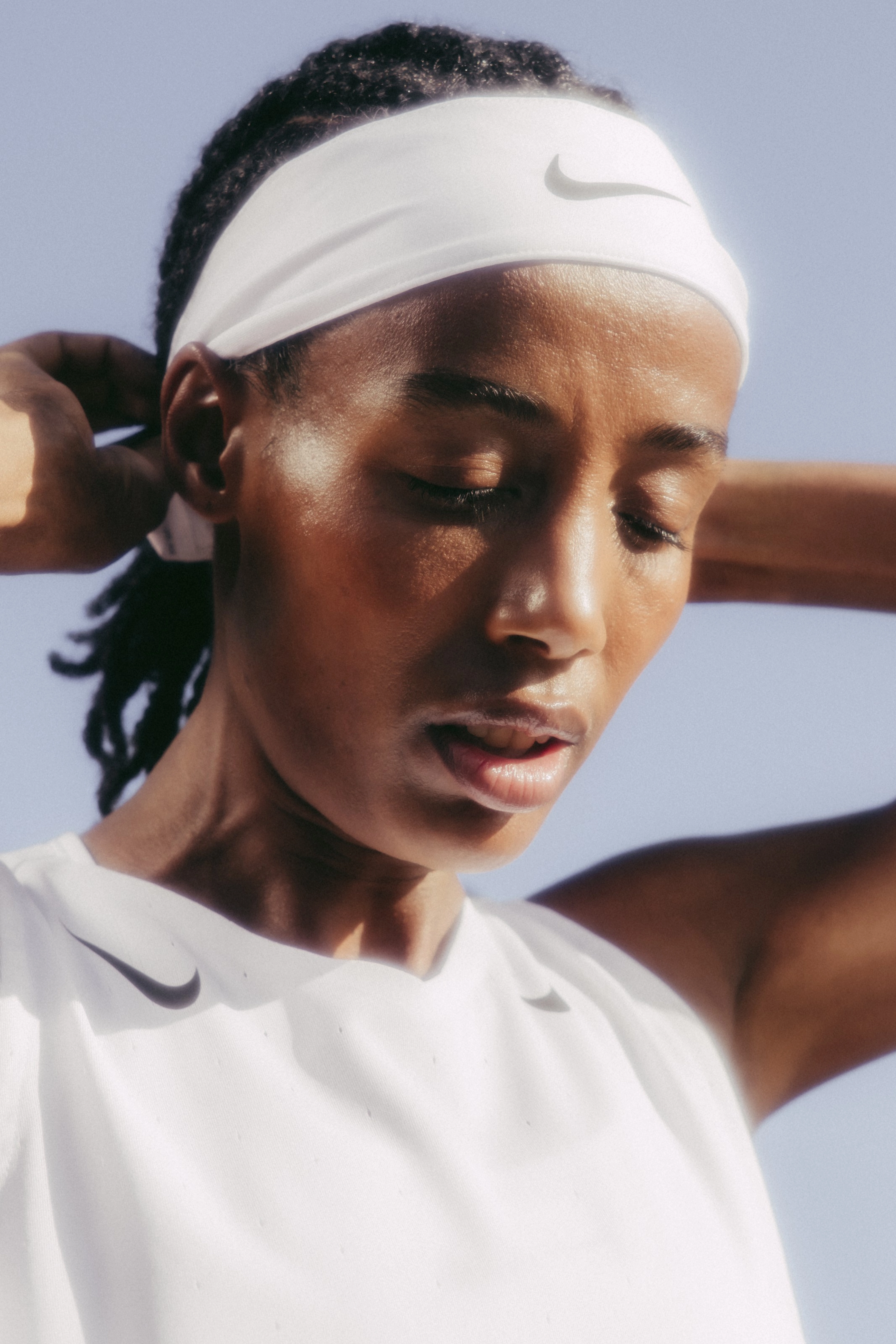 Close up of Sifan Hassan wearing a white Nike running top. She adjusts a white Nike headband over her braided hair.