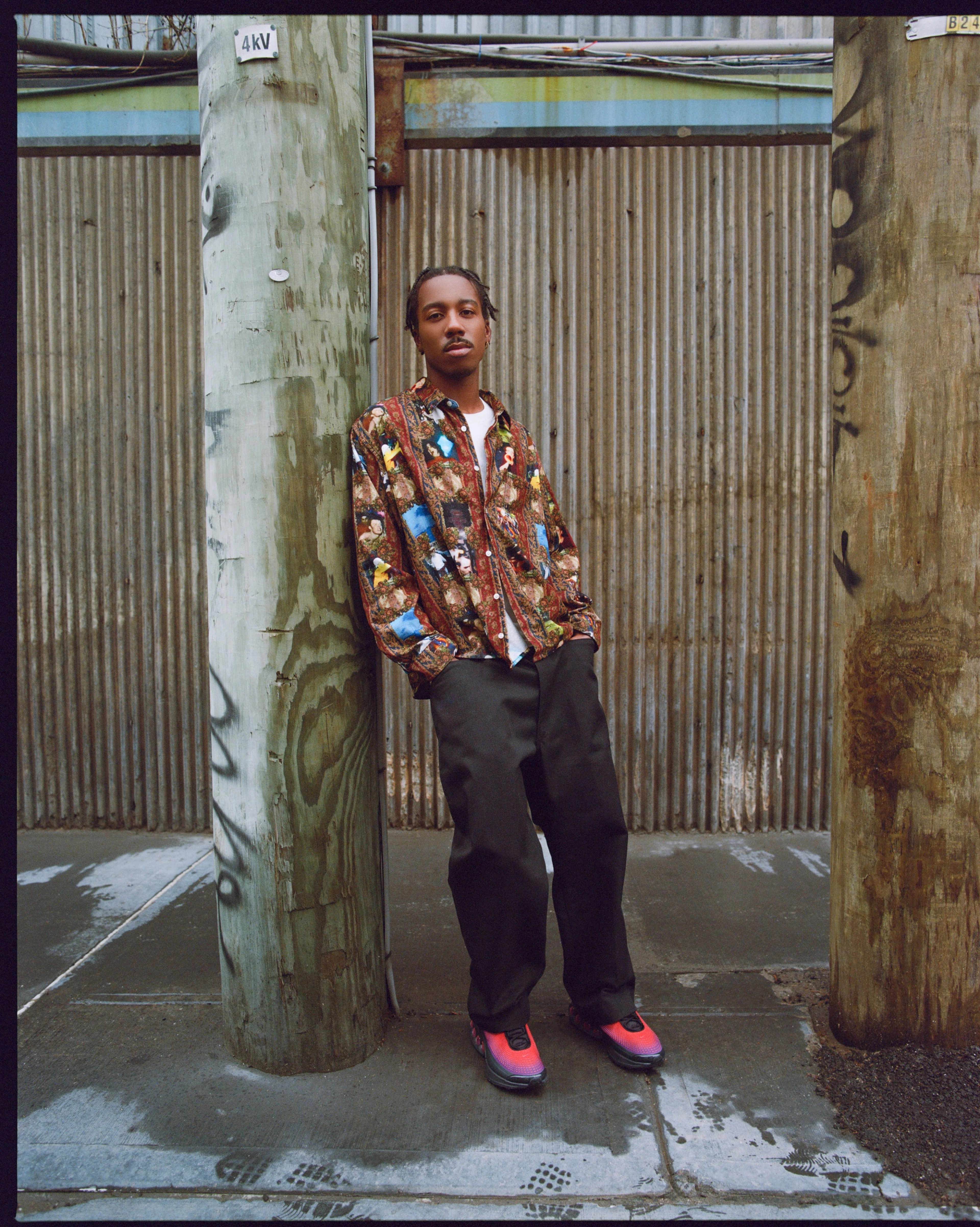 A male model leaning against a telephone pole while wearing the Nike Air Max Dn in black and red