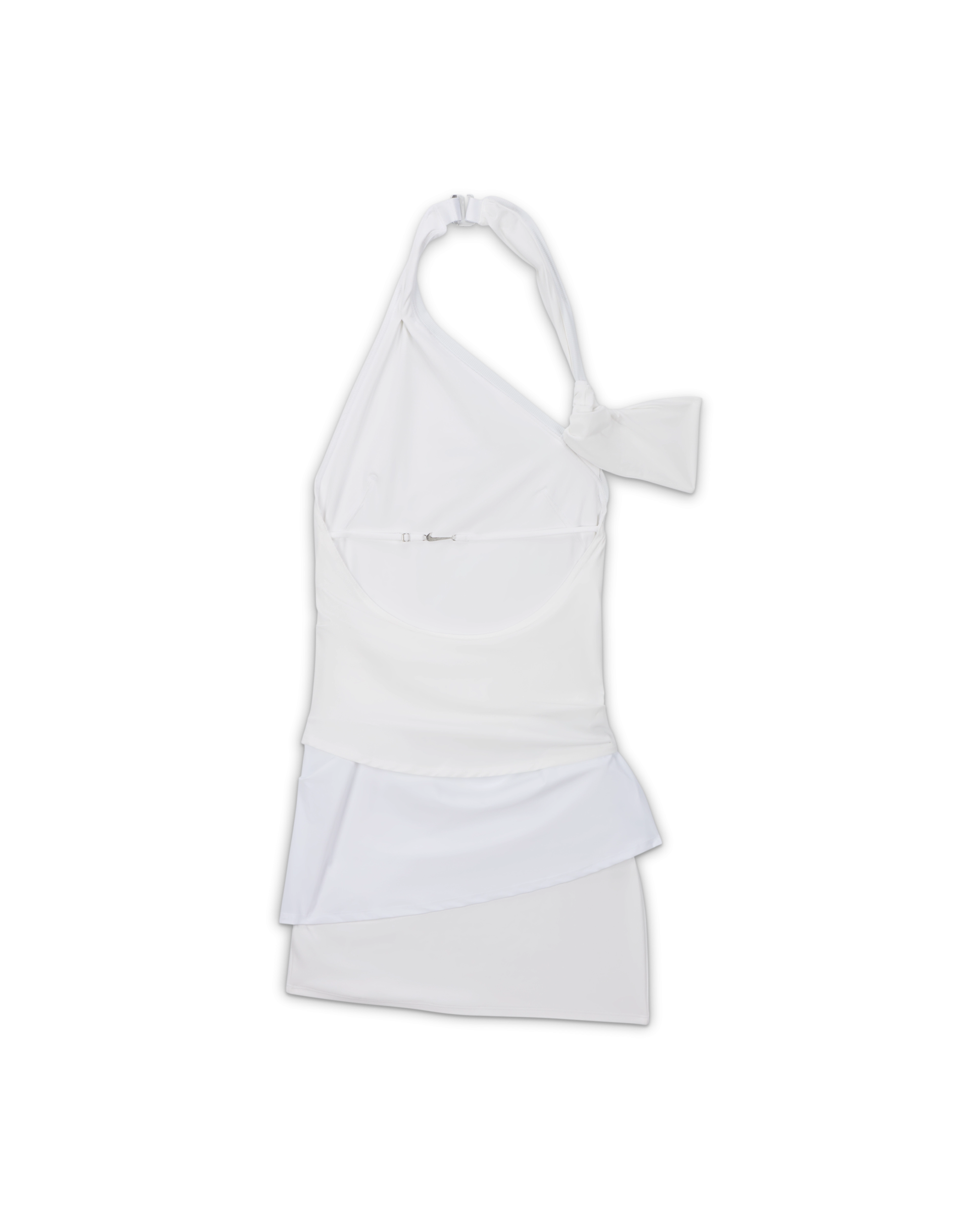 Back overhead view of the Nike x Jacquemus Women's Layered Dress in white. The form fitting, stretch dress hits at mid to upper thigh, and is sleeveless. There is a strap that attaches at the back of the neck with a silver closure and a thin strap that attaches across the back with a silver Swoosh closure. The white arm band is positioned to the right. The dress floats on a black background.