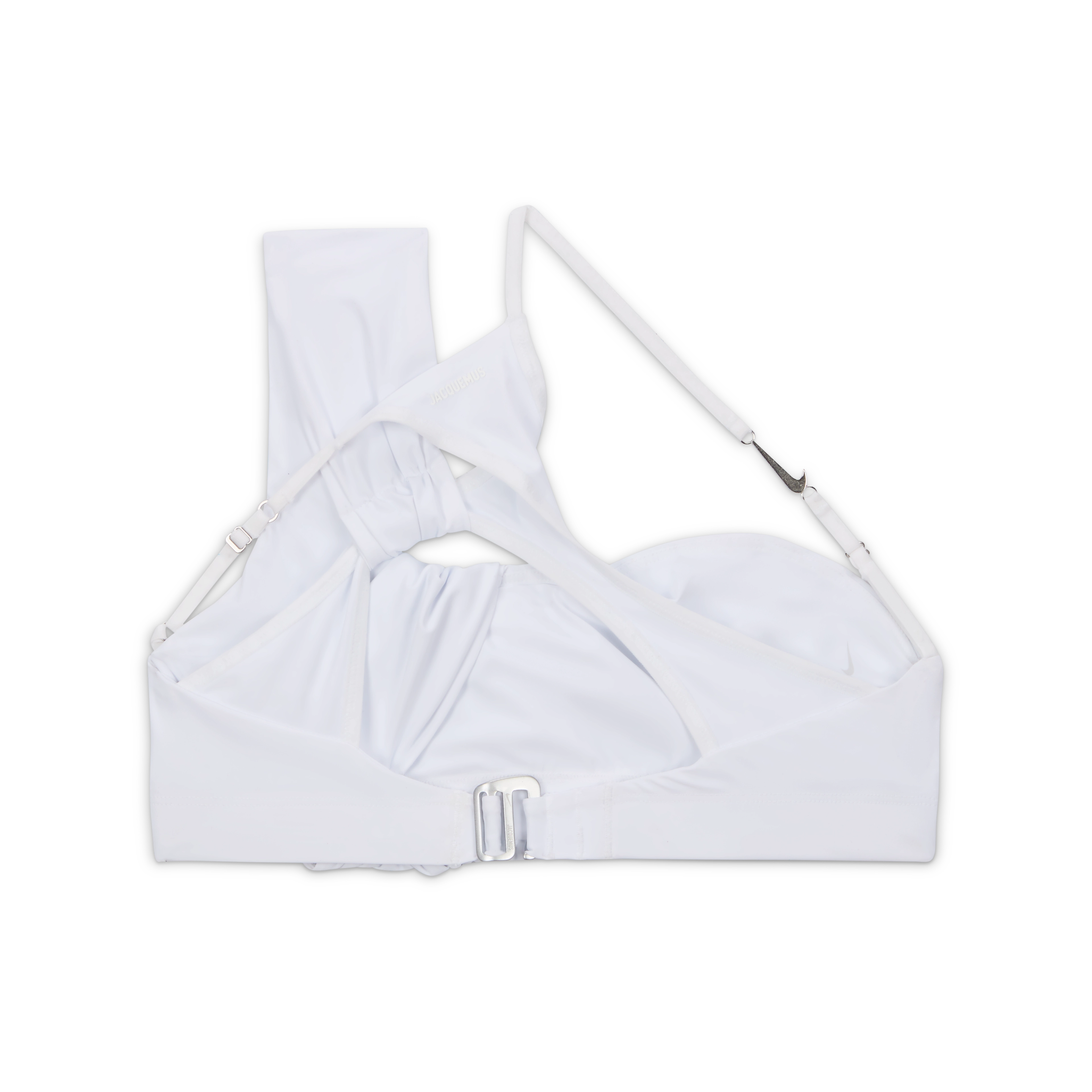 Back overhead view of the Nike x Jacquemus Women's Top in white. A layered, ruched design has one over-the-shoulder strap and one thin cross body strap with a silver Swoosh metal detail. We see the silver metal closure on the back. The top floats on a black background.