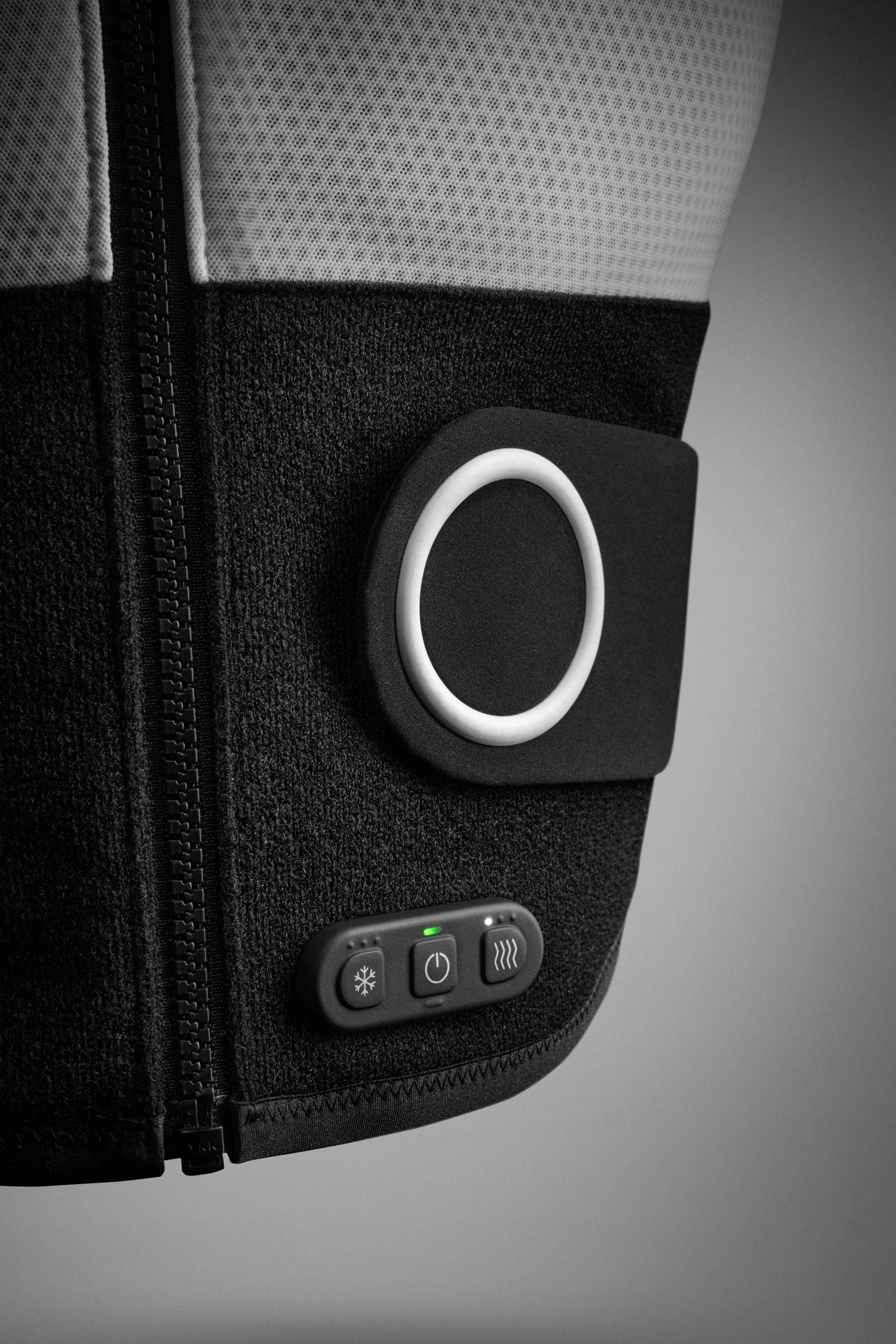 Detail view of Nike x Hyperice Vest control buttons. 3 black buttons sit near vest closure tab, which is black with a white circle detail. White vest sits against a grey background.