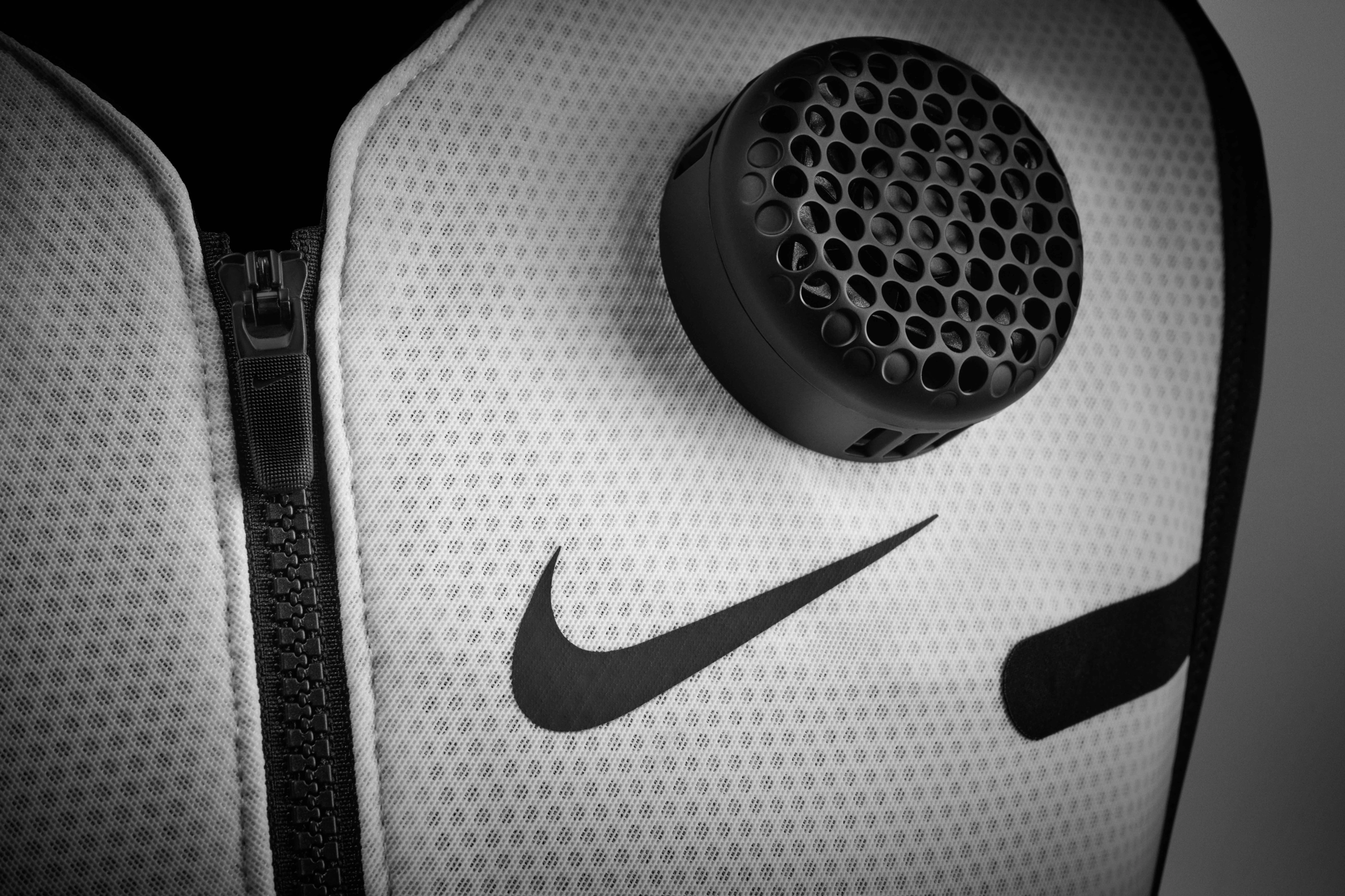 Detail view of a thermal module sitting on the front of a Nike x Hyperice vest, above a black Nike Swoosh. The white vest sits against a grey background.