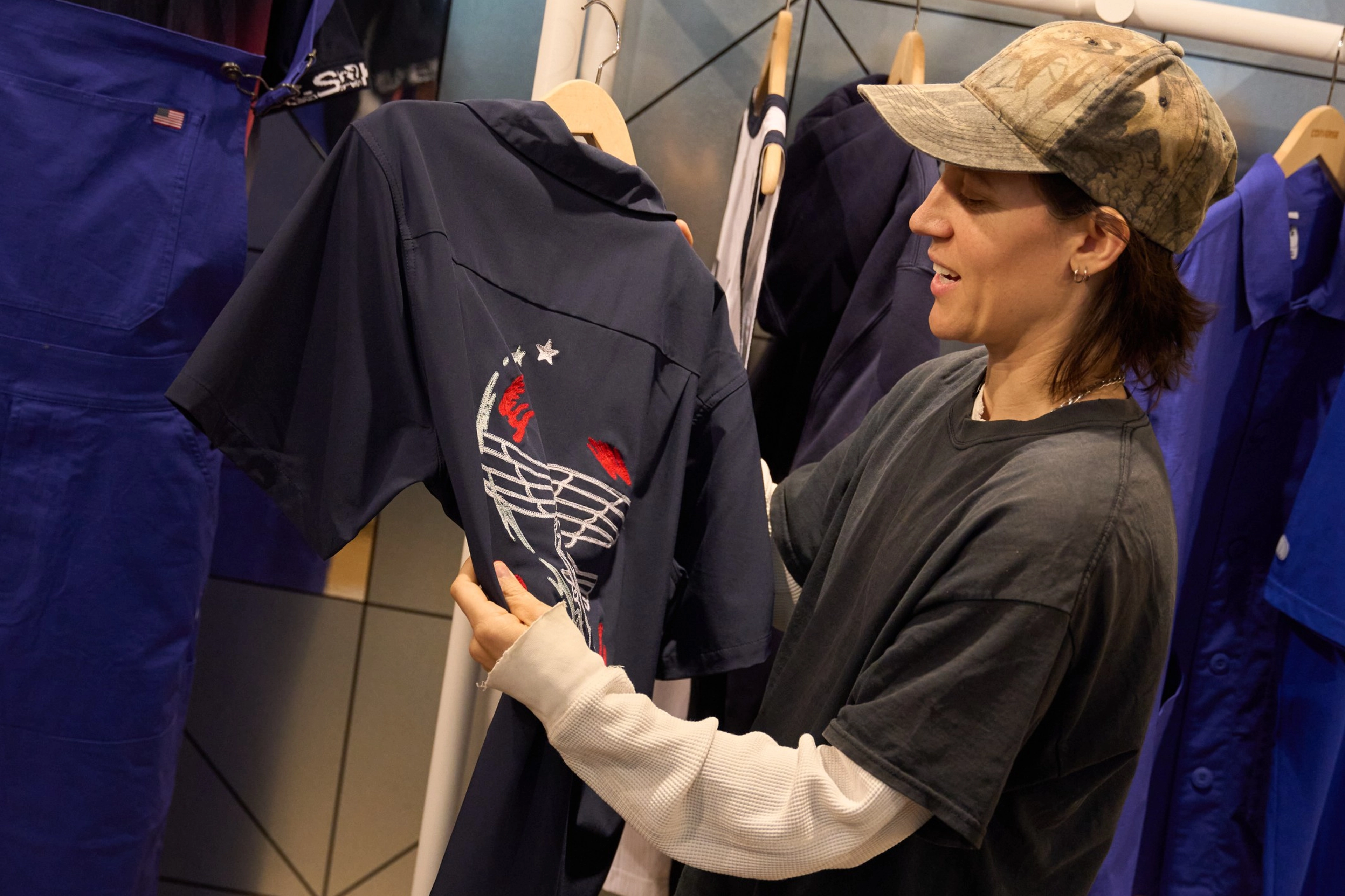 Alexis Sablone holding up a shirt from the skateboarding federation kits surrounded by racks of other apparel items from the federation kits.