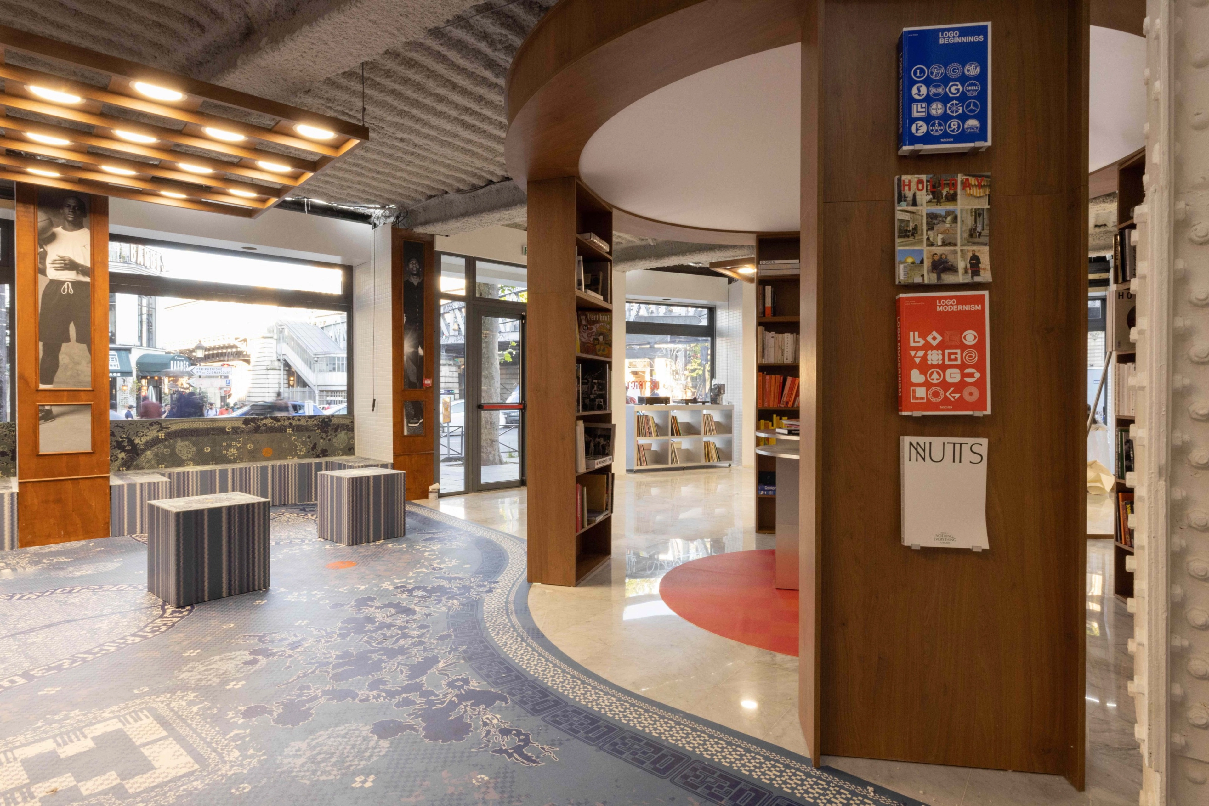 Indoor photo of the District 23 library. On the right are bookcases arranged in a circle and on the left is an open seating area with artistic patterns and photos of athletes.