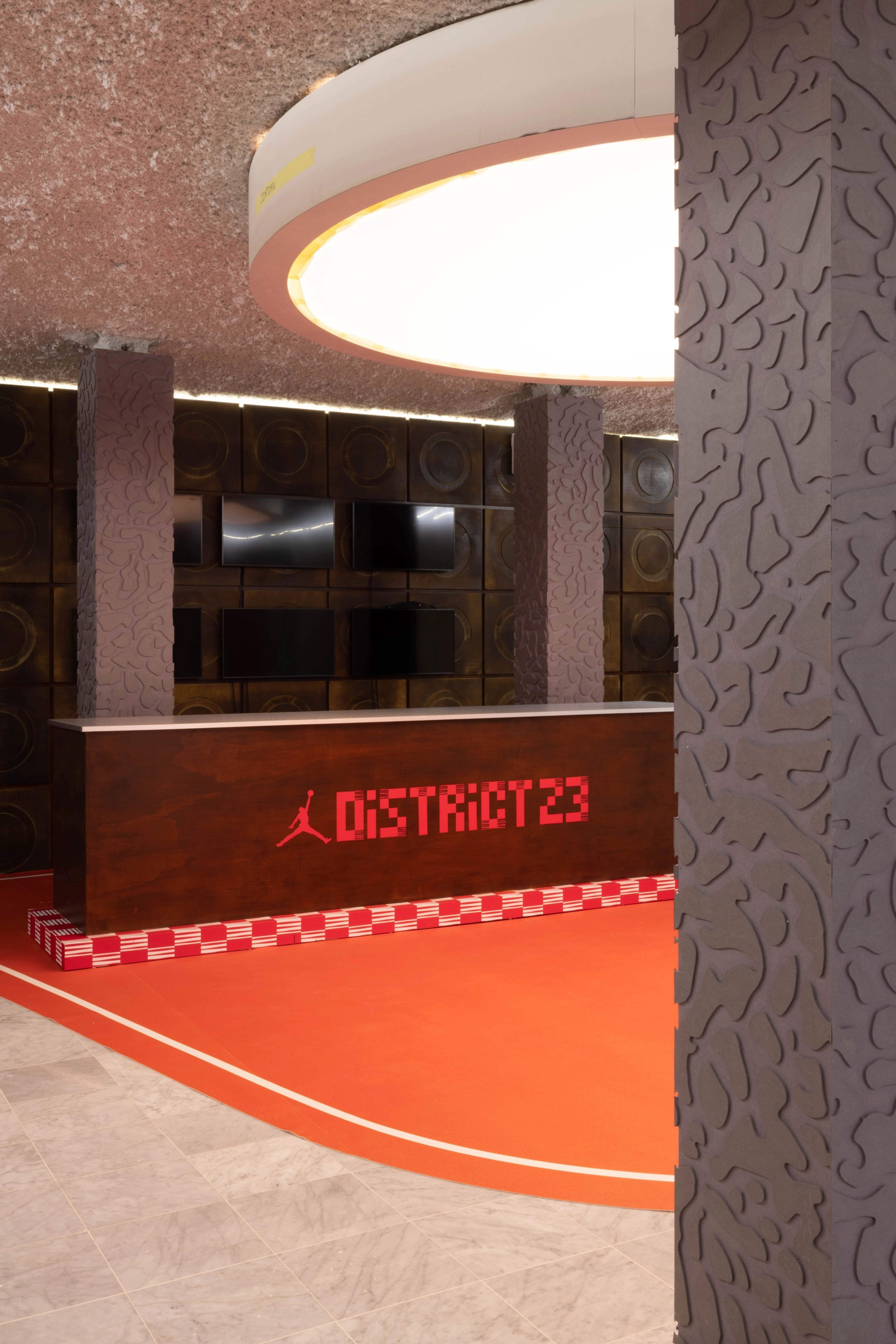 Side angle view of the District 23 main entrance area, offering a close-up view of the embossed knockdown wall pattern on the support columns.