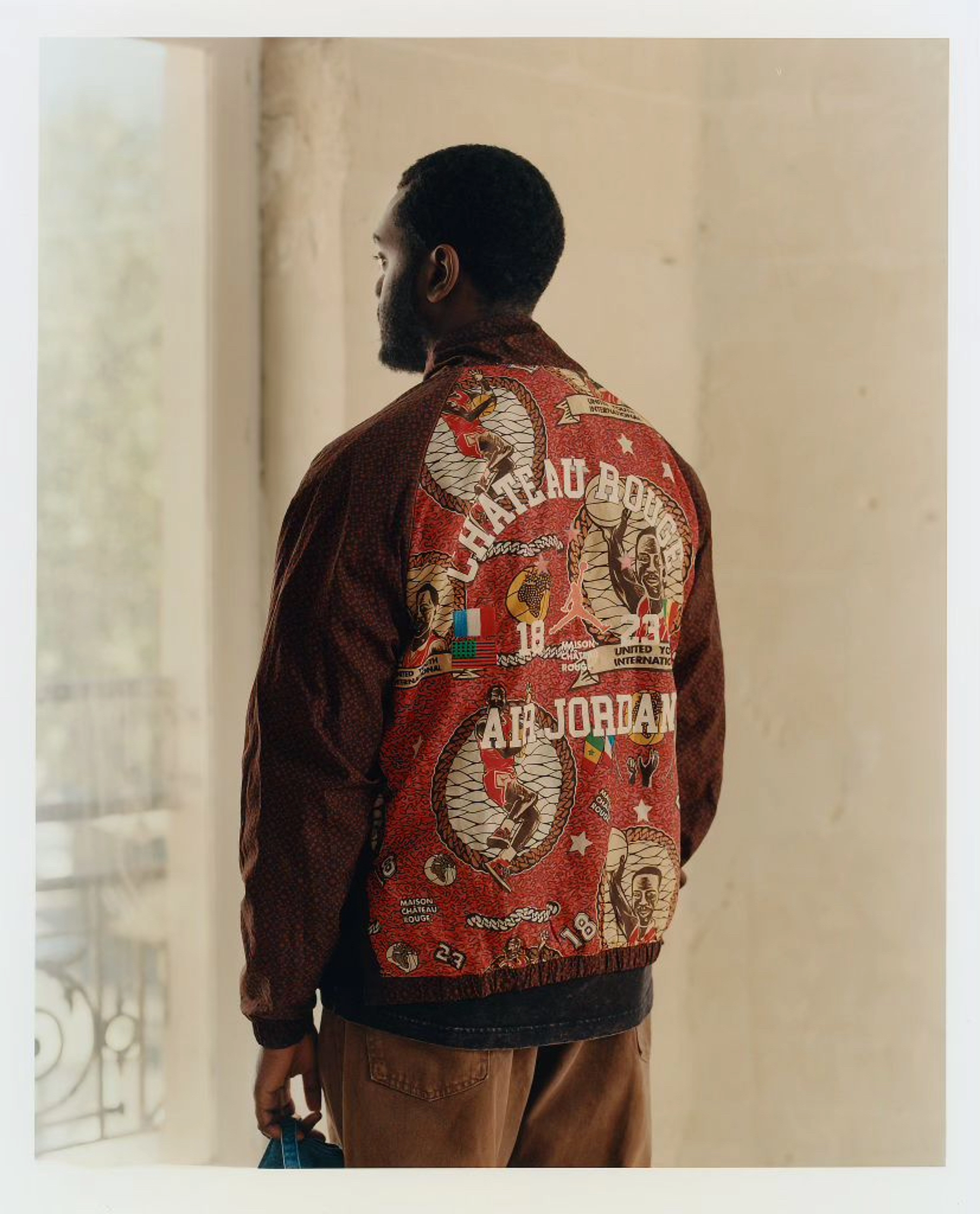 Back angle view of Youssouf Fofana wearing a Chateau Rouge Air Jordan jacket and looking out a window.