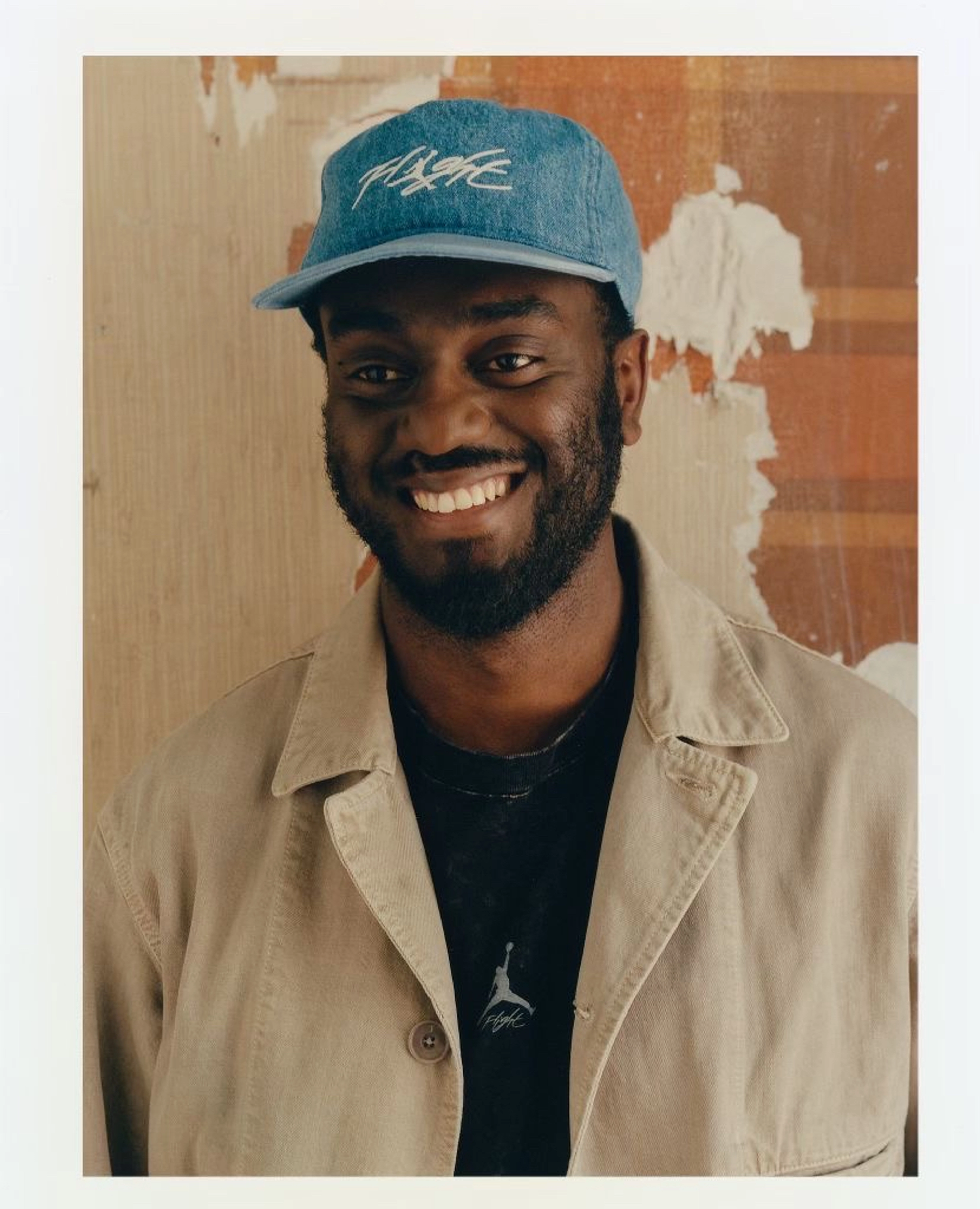 Youssouf Fofana smiling and wearing a denim Air Jordan baseball cap, a tan jacket, and a black Air Jordan shirt.