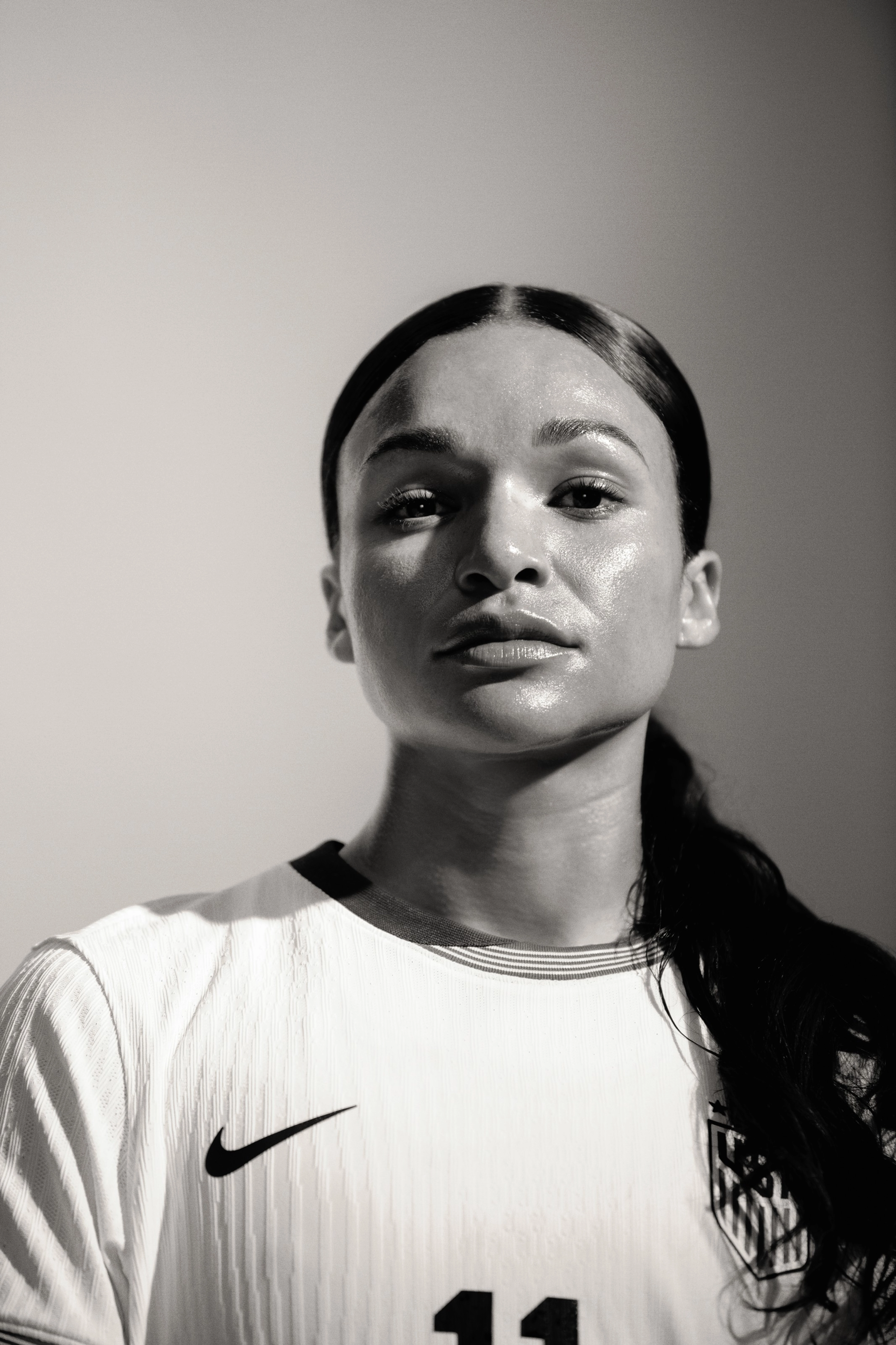Black and white close up of Sophia Smith wearing a white Team USA football jersey, looking directly at the camera. Her hair is pulled back into a ponytail.