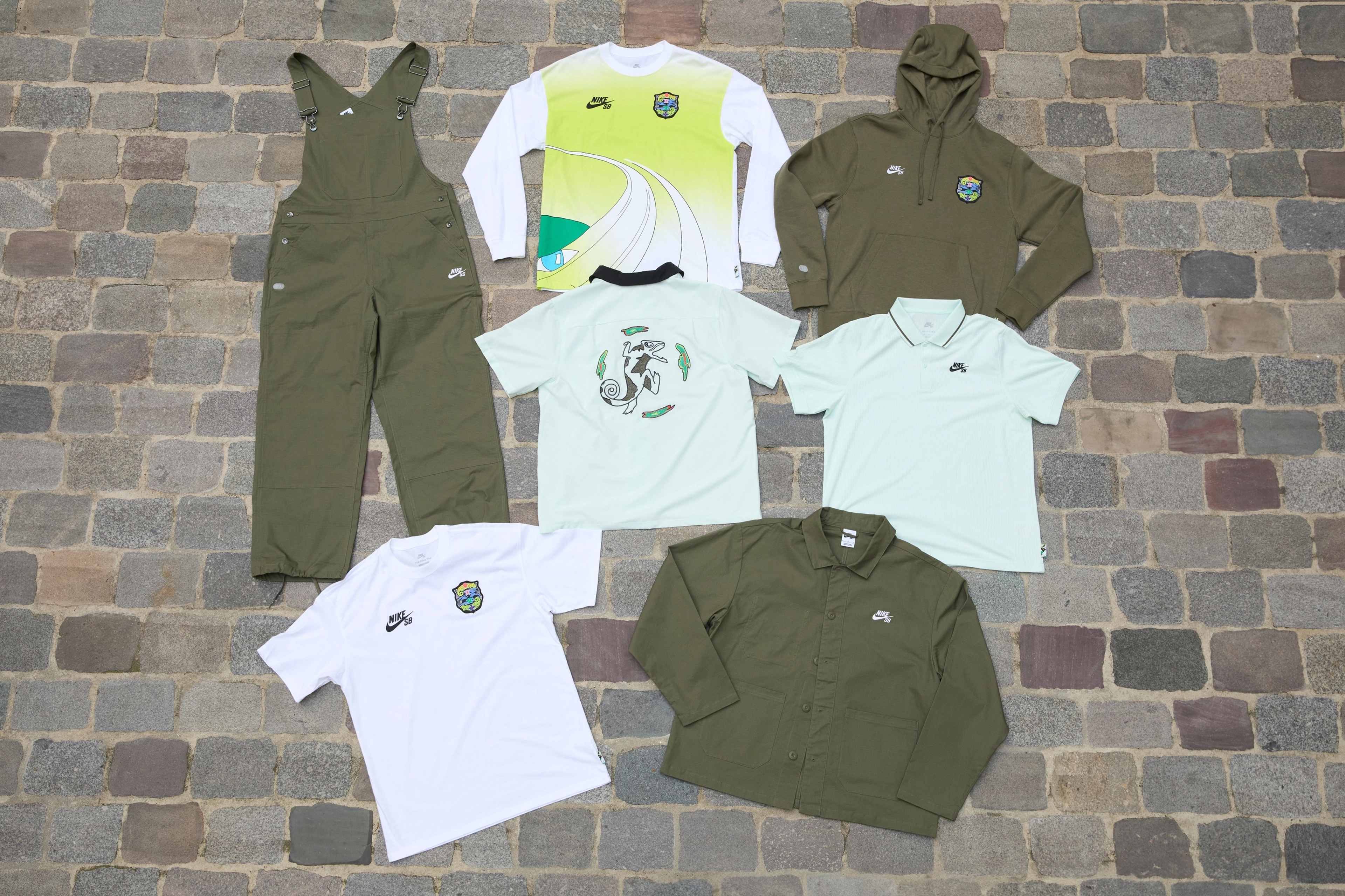 Overhead view of 7 clothing items from the skateboarding federation kits that feature a crest designed with a pair of chameleons connected by a wavy illustration of earth and centered with four unique species of orchids.