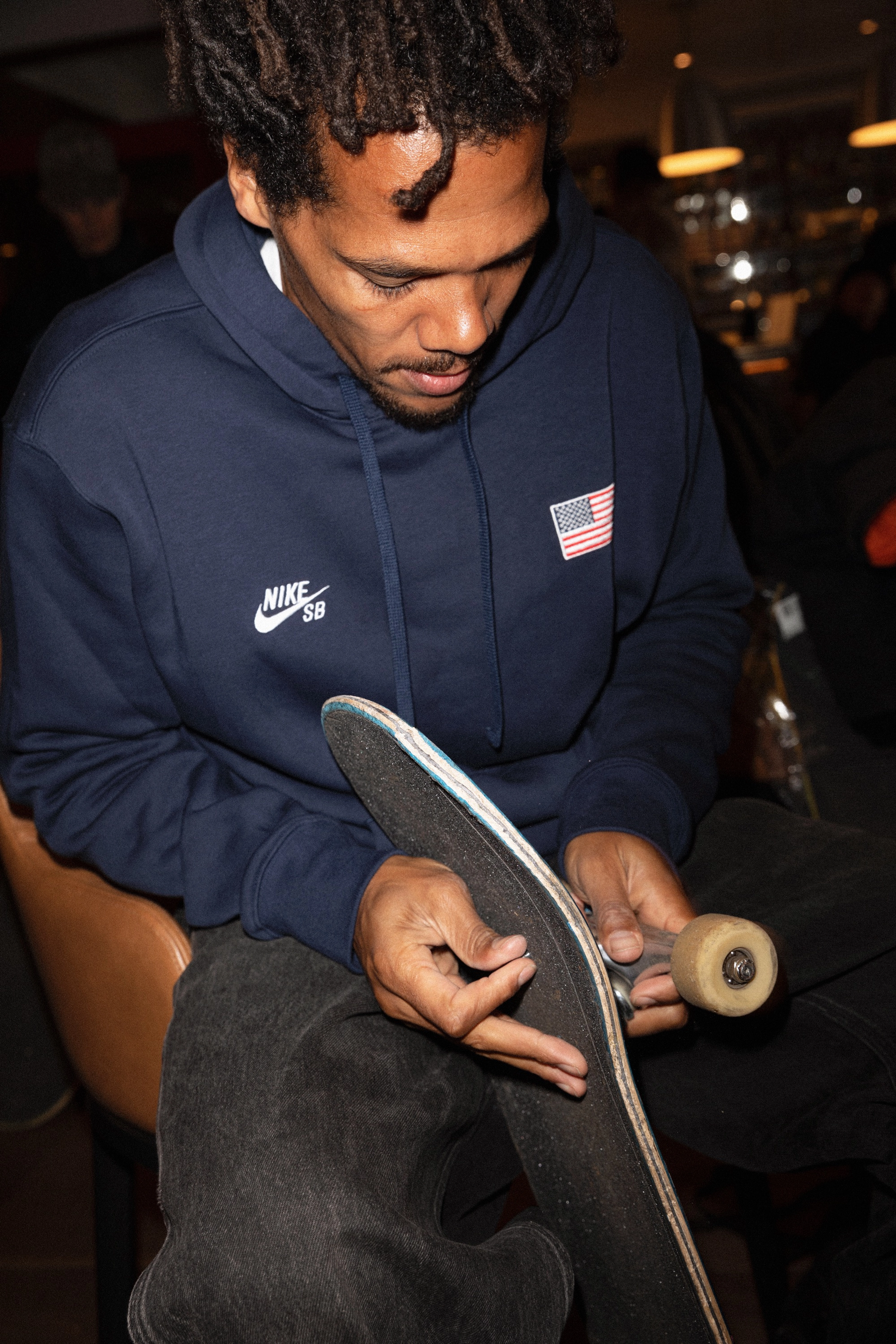 Nike SB team rider Korahn Gayle wears a hoodie from the USA skateboarding federation collection and holding a skateboard.