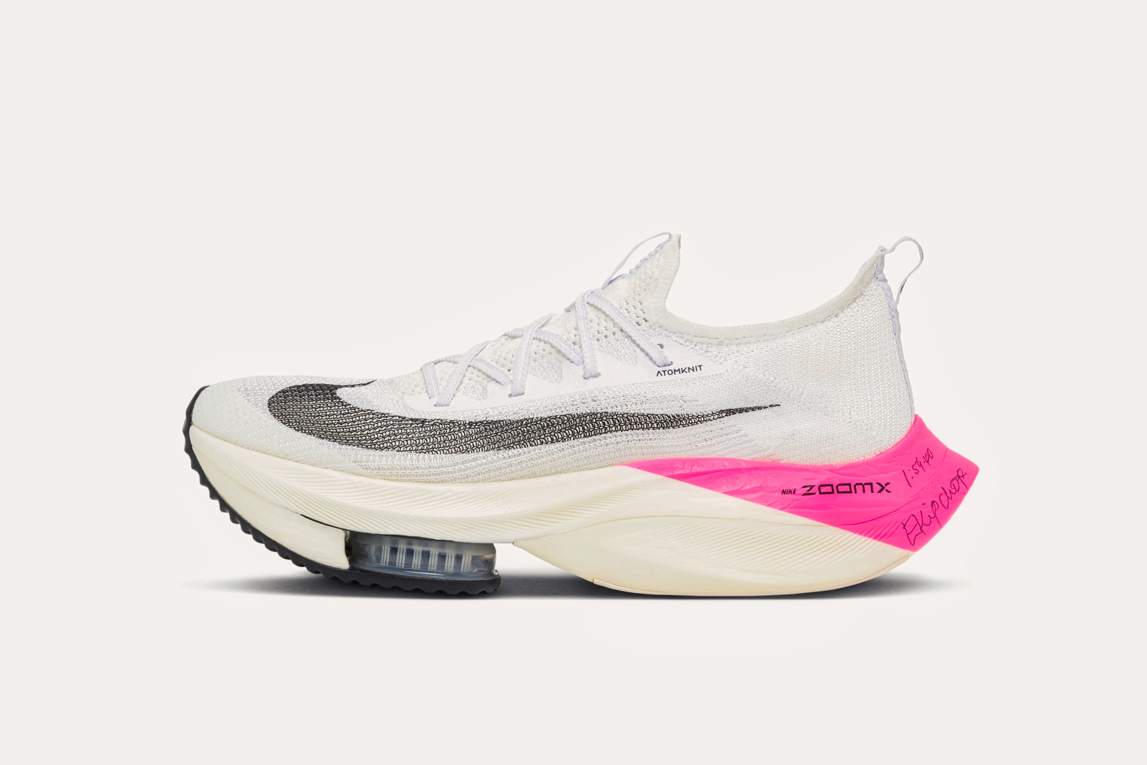 A white sneaker with a grey swoosh on the front and a pink heel in the back that has "ZOOMX" printed on it and Eliud Kipchoge's signature written on it in pen.