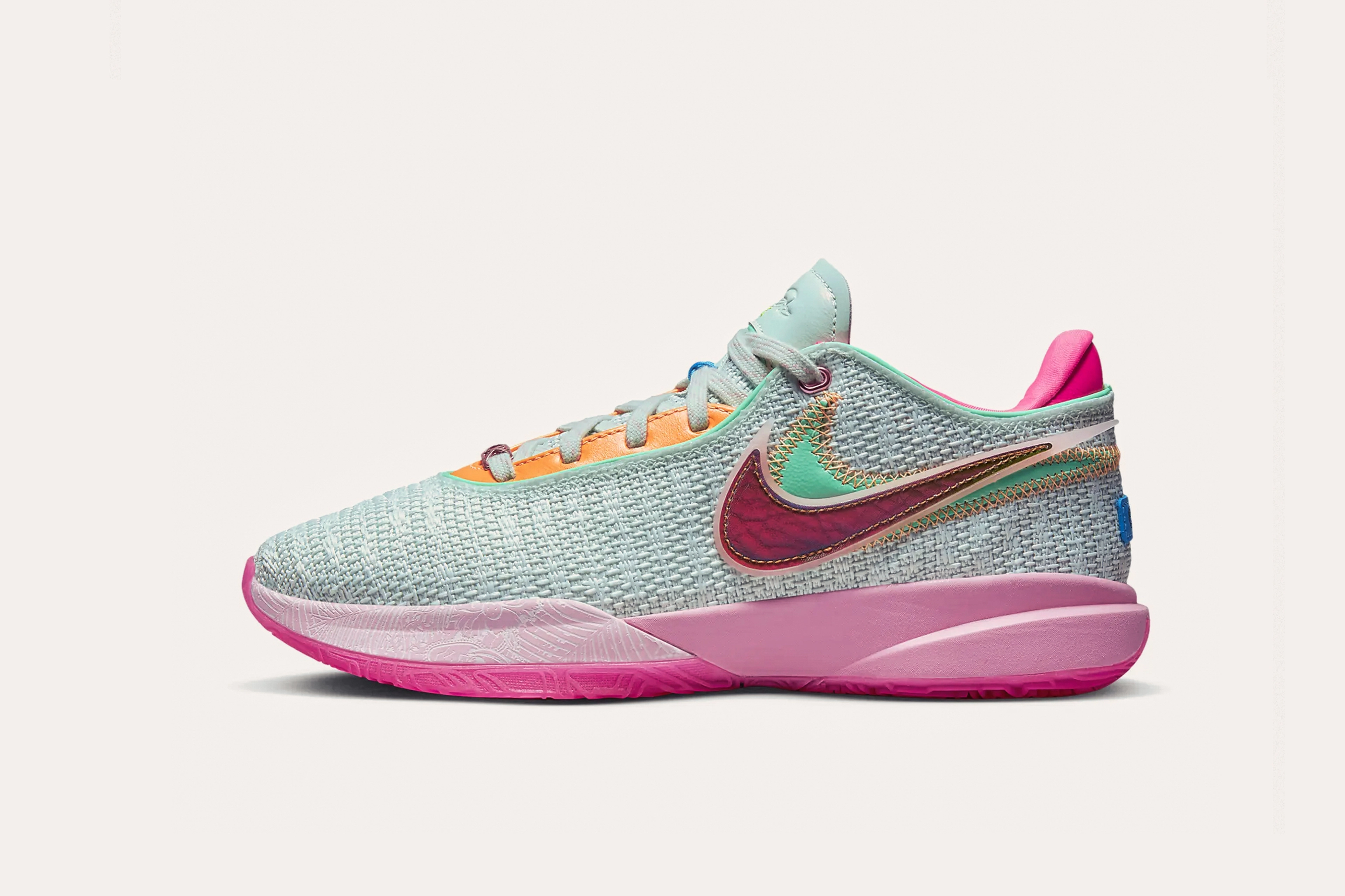 A light teal sneaker with a maroon Nike swoosh layered on top of a teal swoosh on the side, orange shoelace tabs, a pink sole, and a pink rear cuff.