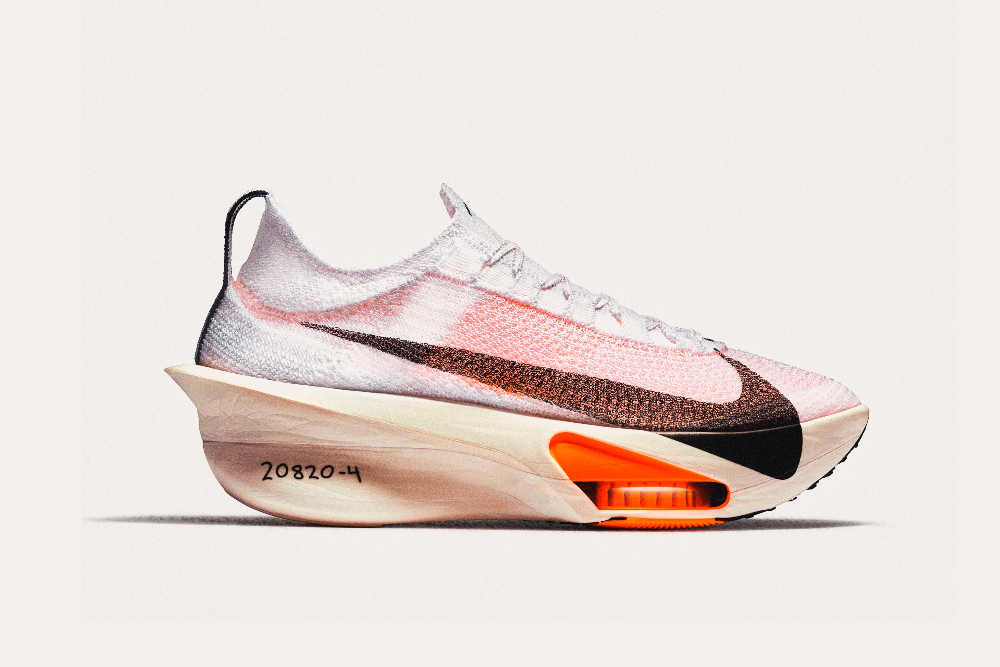 A white sneaker with orange tint, a black swoosh on the side, a neon orange sole support, and "20820-4" written in pen on the heel.