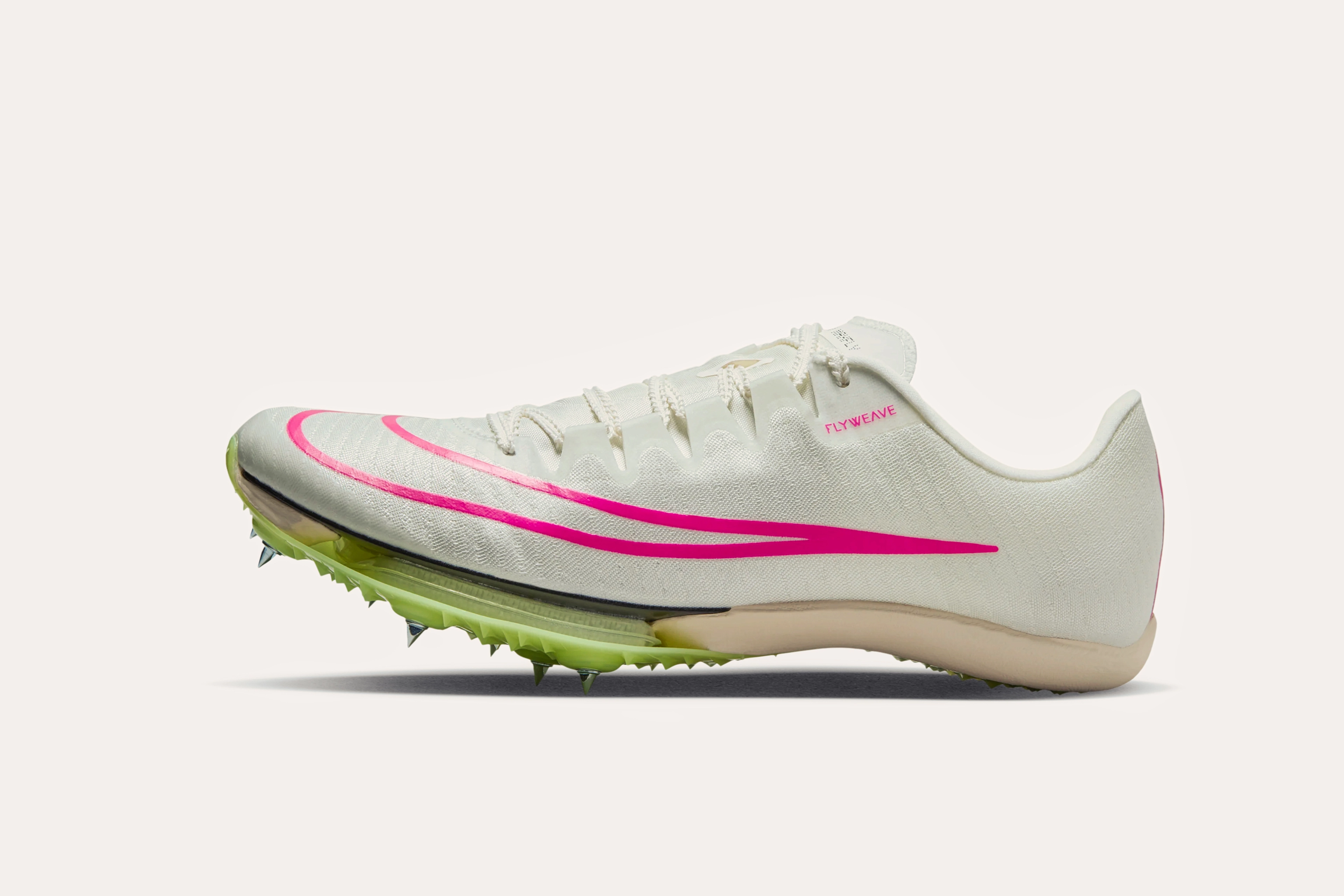 A white sneaker with "Flyweave" printed by the front of the cuff, a pink outline of a Nike swoosh, and a light green sole with spiked cleats.