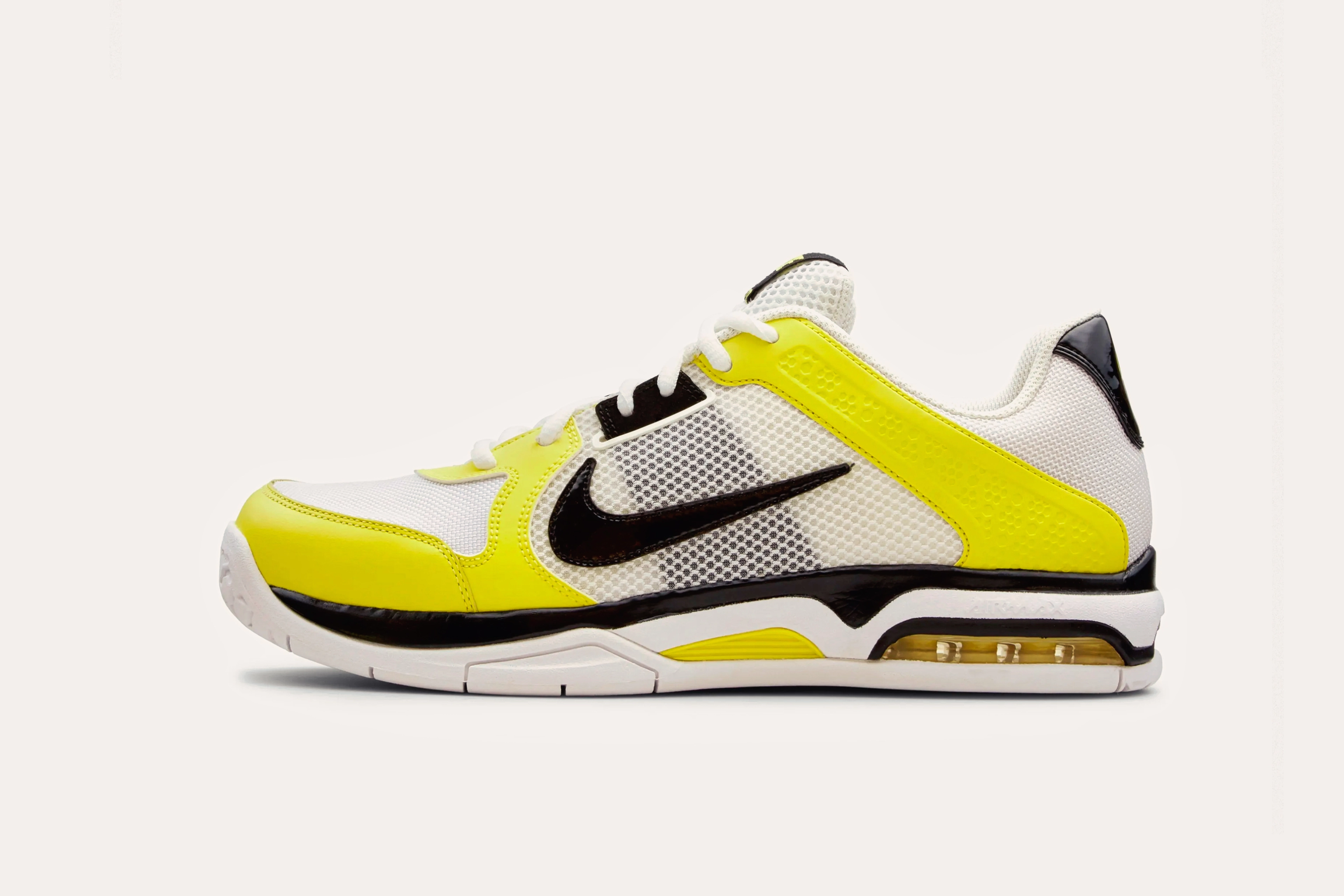 A white sneaker with a black Nike swoosh on the side mesh, a bright yellow stripe across the toe and heel, and a bright yellow toecap.