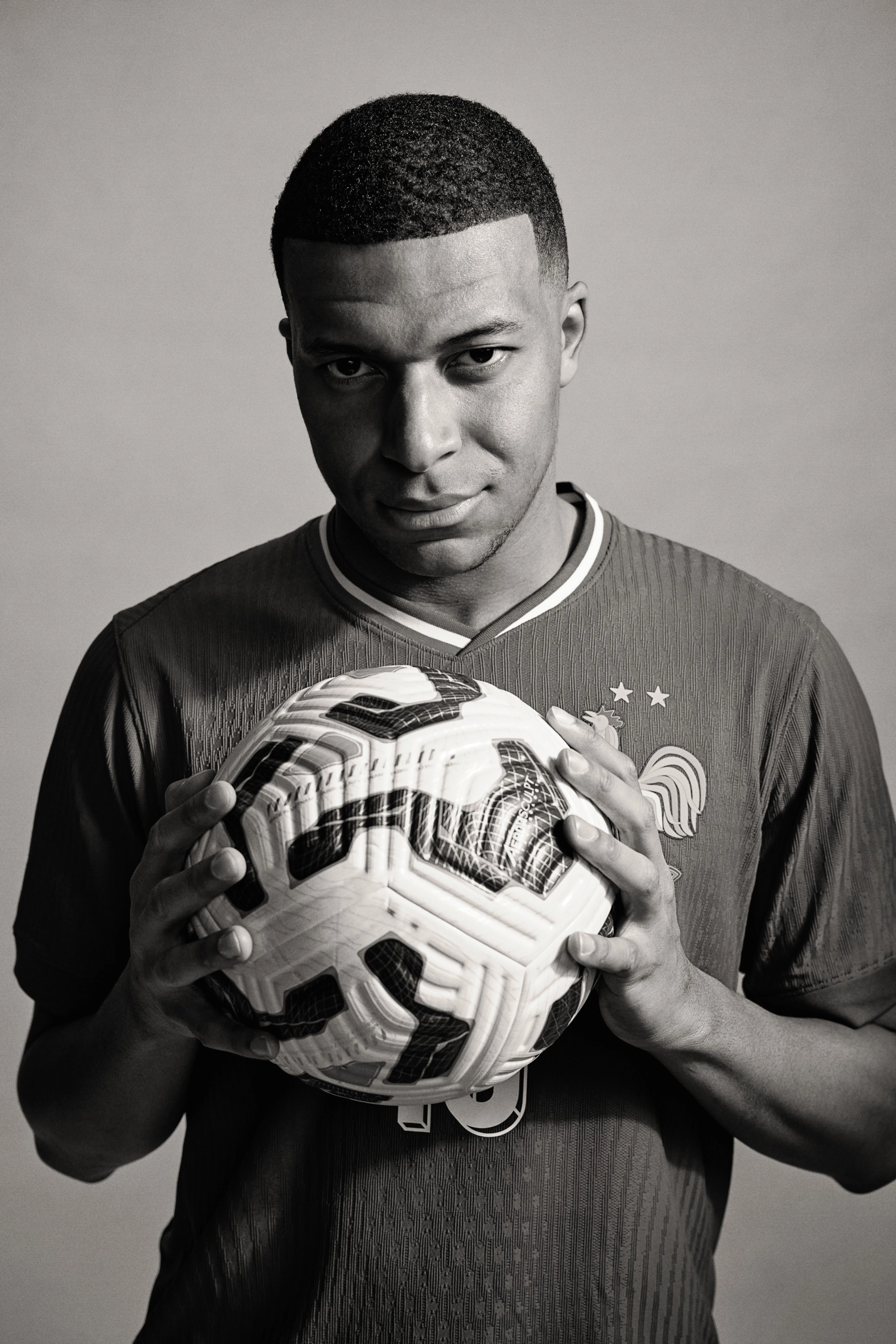 Black and white photo of Kylian Mbappé holding a soccer ball.