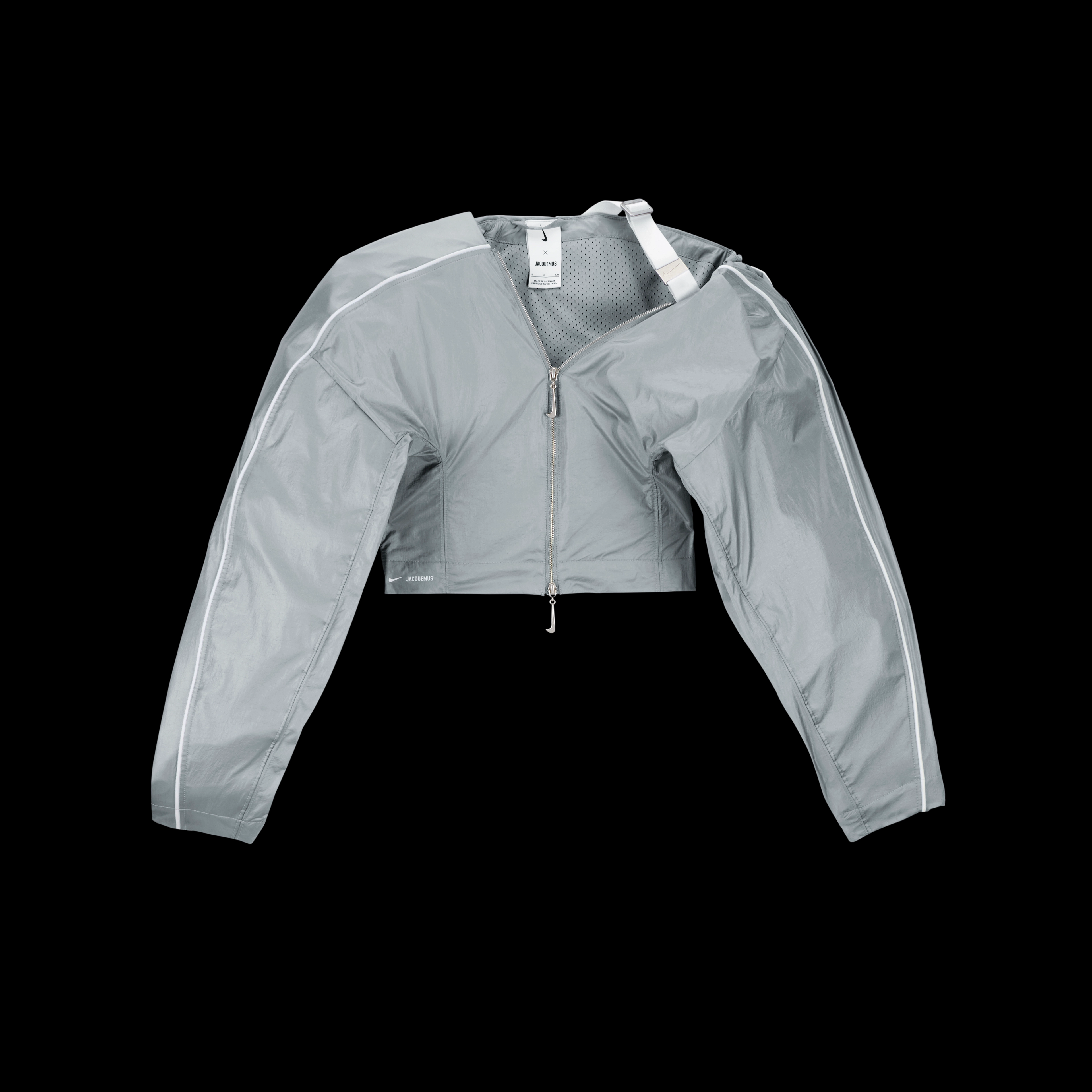 Overhead view of the Nike x Jacquemus Women's Track Jacket in particle grey with white pinstripes across the shoulder and down the sleeve. One sleeve is oversized and attached to the back of the jacket with white webbing. The jacket zipper pull is grey in the shape of a Nike Swoosh. The piece floats on a black background.