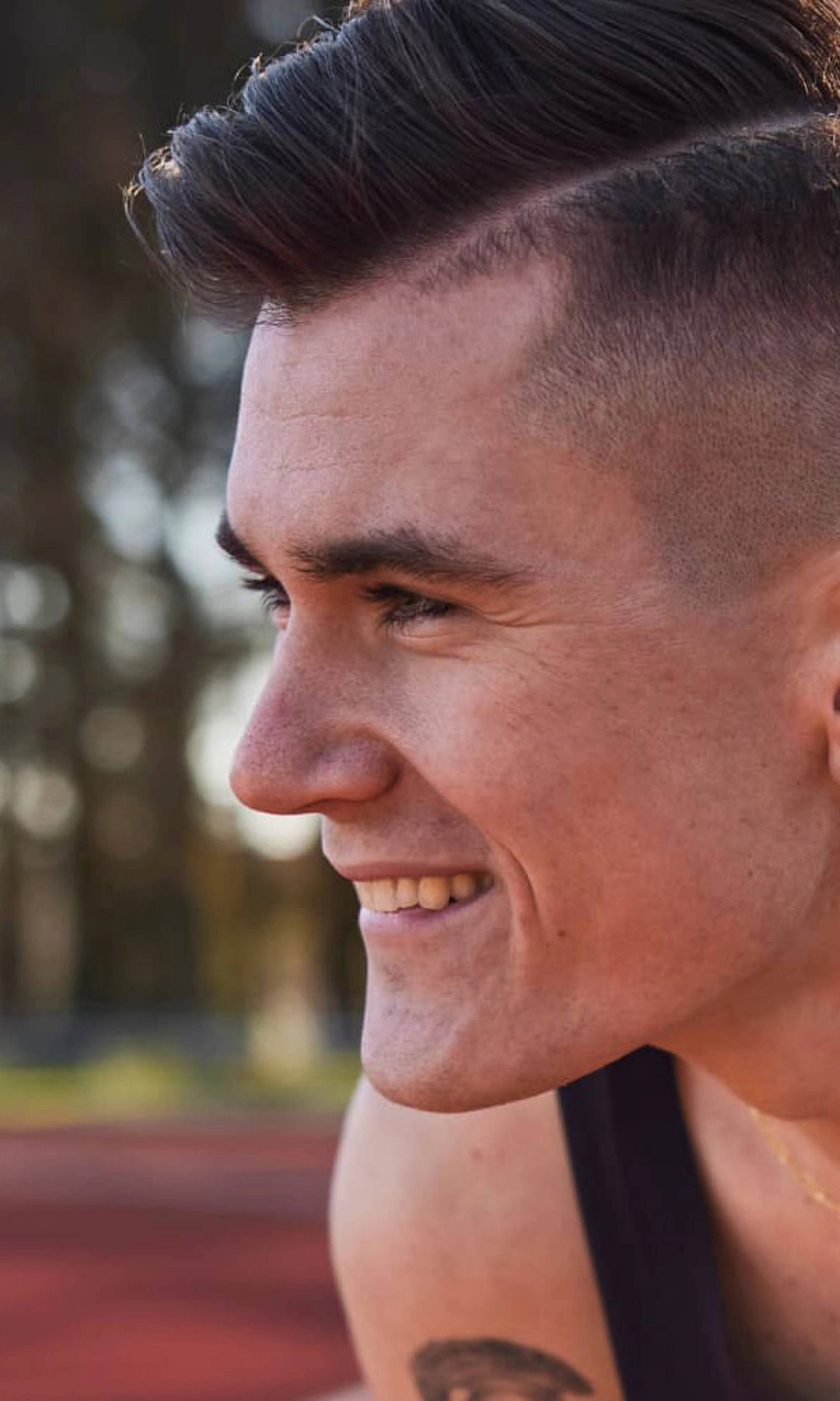 Jakob Ingebrigtsen, crouches on a track, and smiles as he looks to the left, wearing a black Nike singlet and a gold chain around his neck.