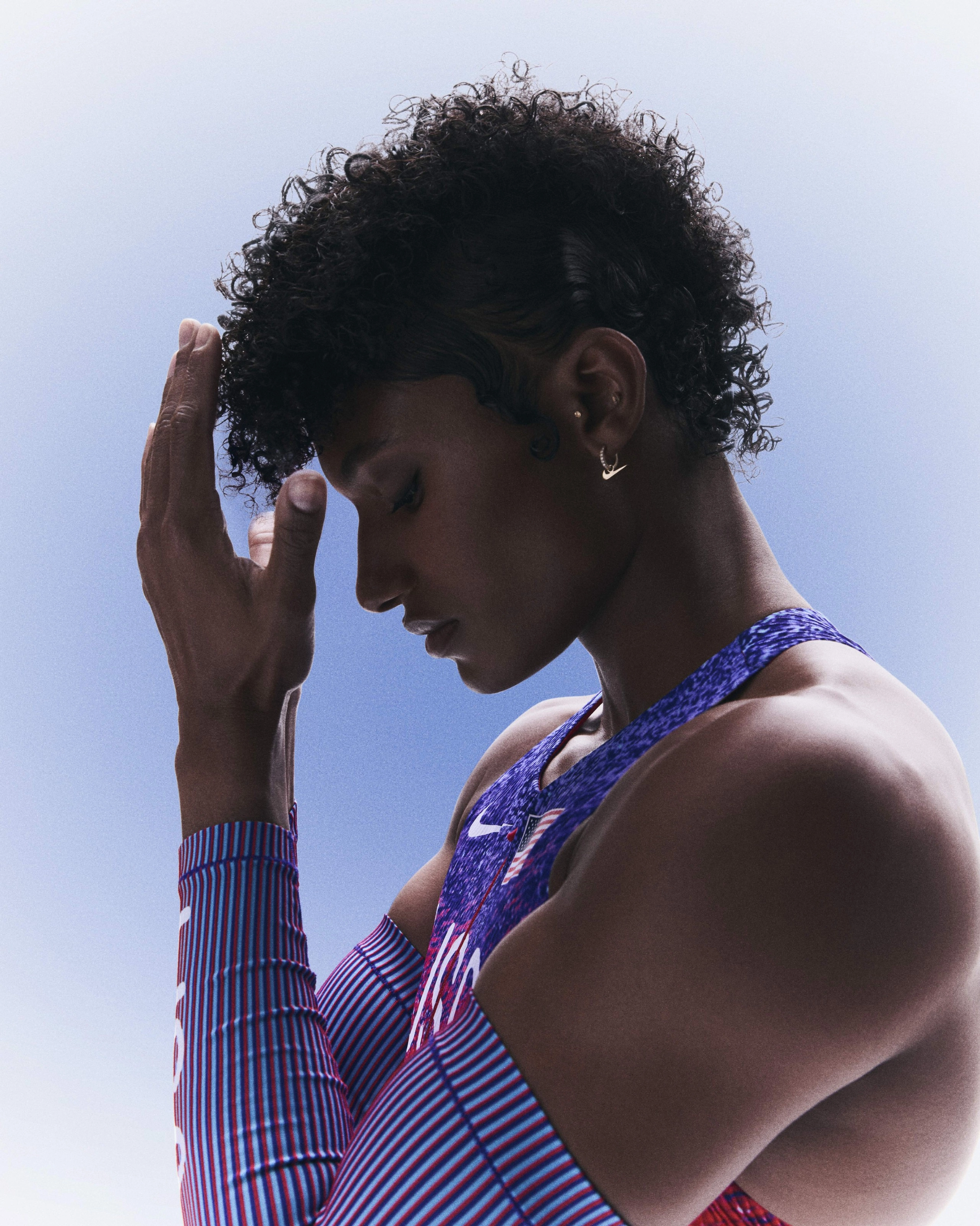 Profile upper body view of Anna Cockrell with her hands hovering over her face and wearing her track and field kit uniform.