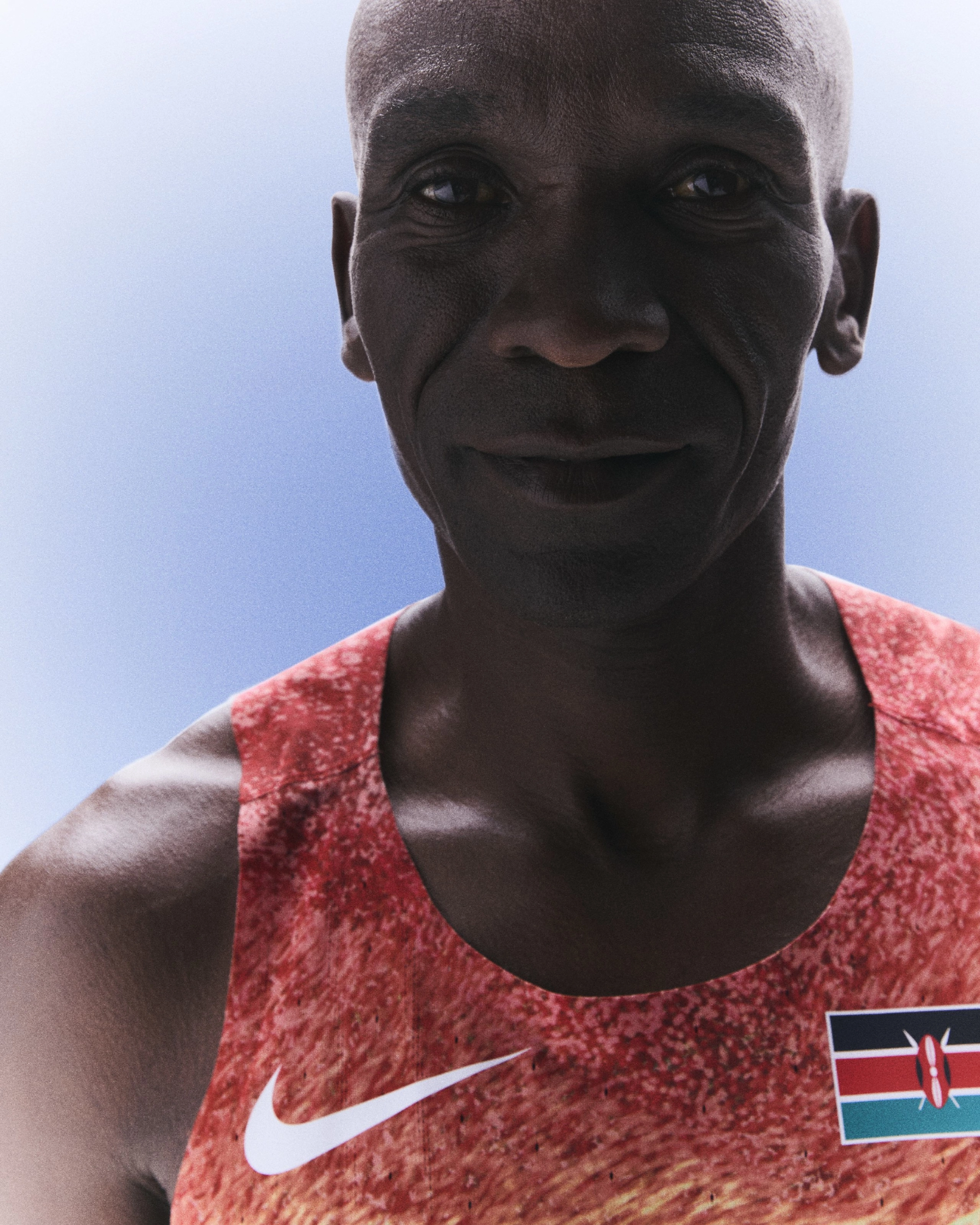 Front upper body view of Eliud Kipchoge smiling and wearing his Kenya track and field kit uniform.